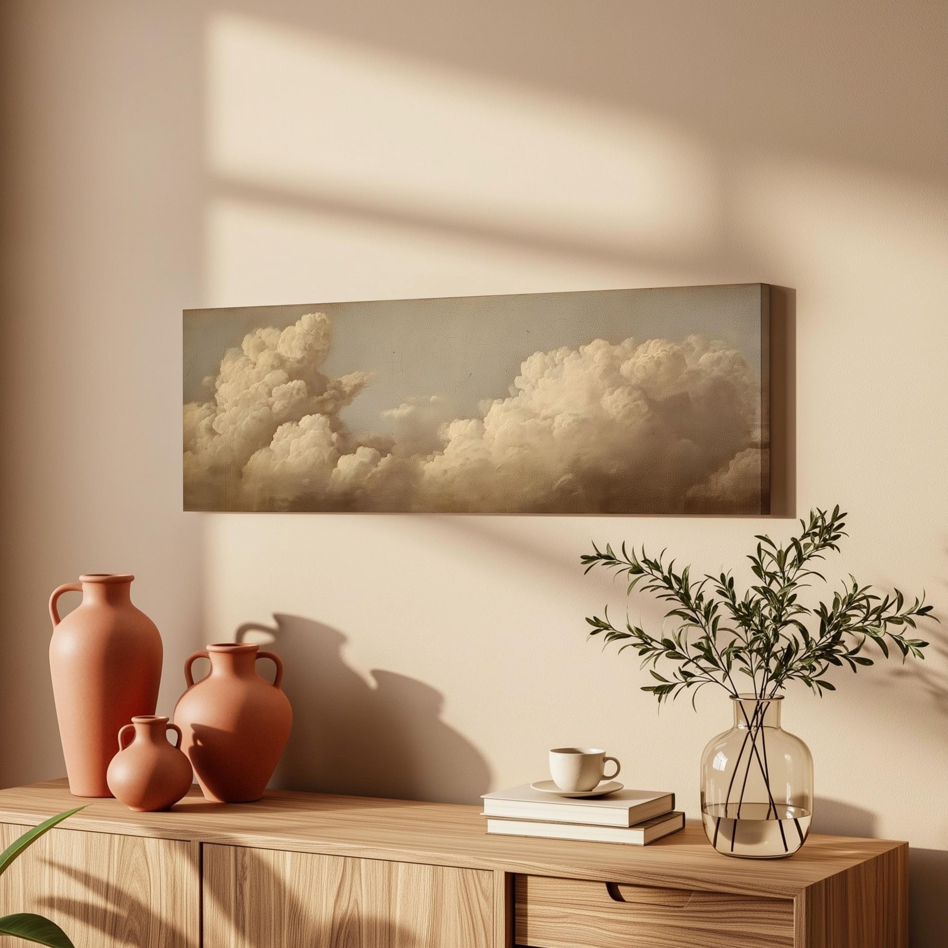 a wooden cabinet with a vase, a plant, and a book on top of it, along with a framed painting of clouds hanging on the wall above.