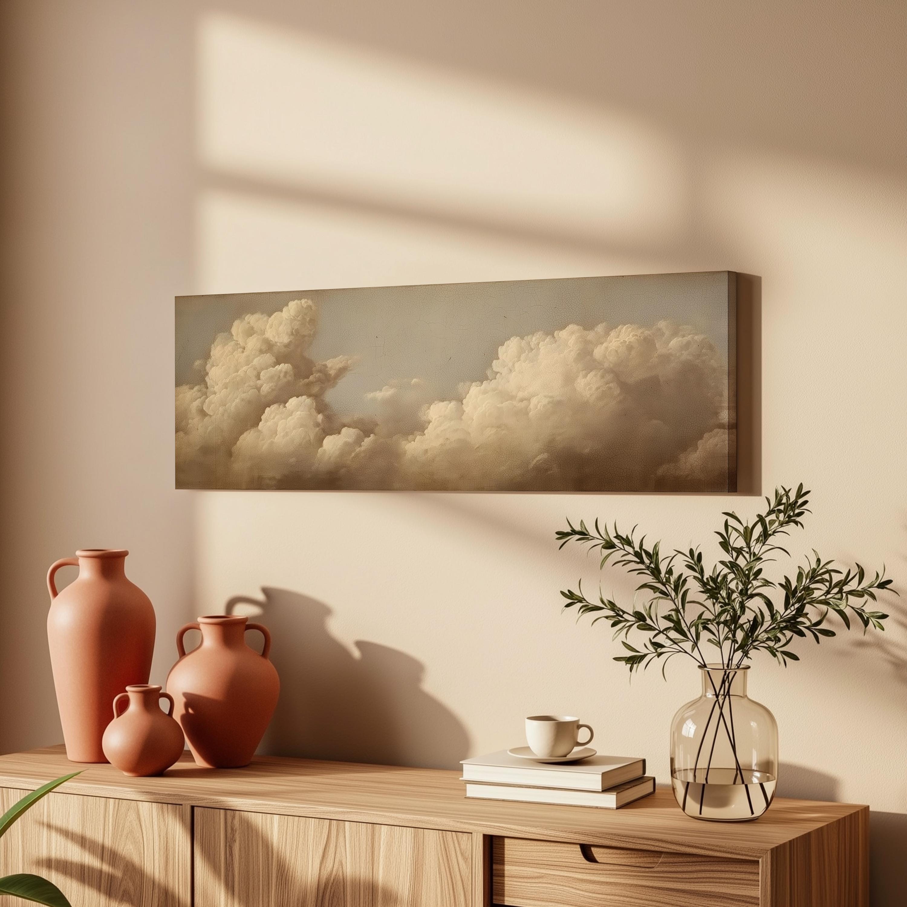a wooden cabinet with a vase, a plant, and a book on top of it, along with a framed painting of clouds hanging on the wall above.