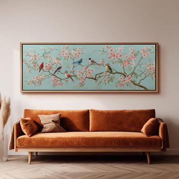 a large, framed painting of a cherry blossom tree with birds perched on its branches, hanging on a wall above a brown sofa.