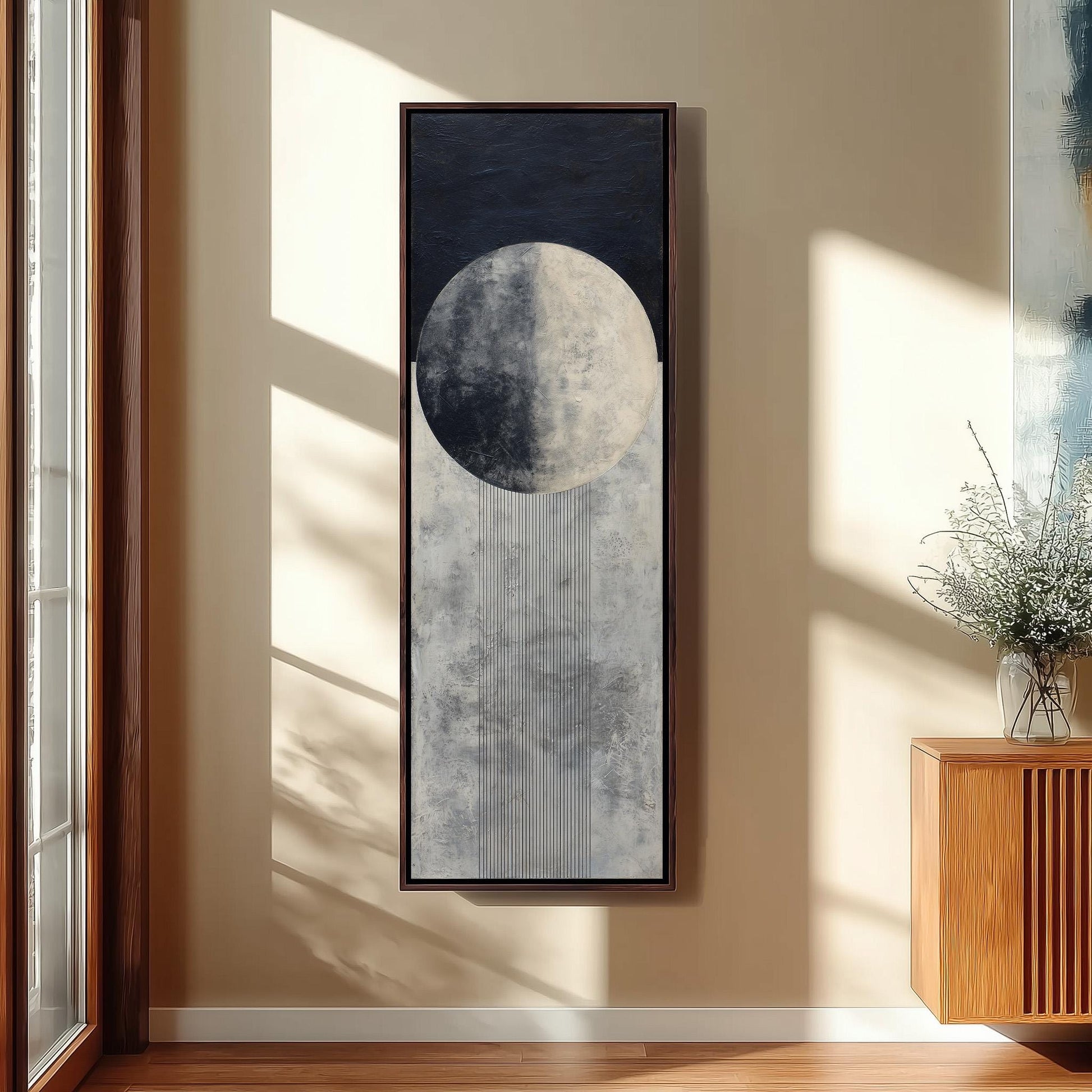 a large framed artwork depicting a moon with a crescent shape, hanging on a wall in a room with a wooden cabinet and a vase of flowers.