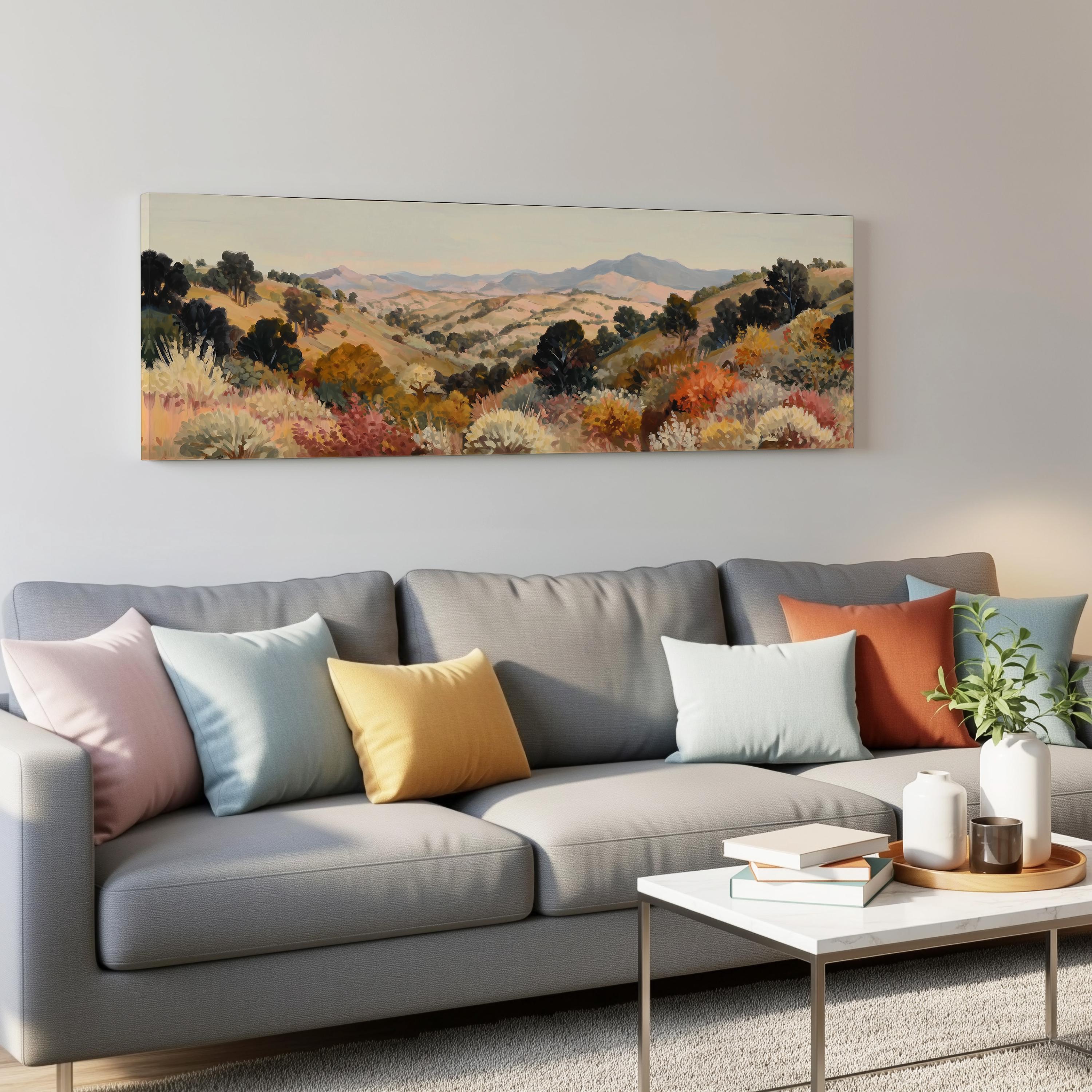 a living room with a gray sofa adorned with colorful throw pillows, a coffee table with books and a plant, and a large landscape painting hanging on the wall above the sofa.