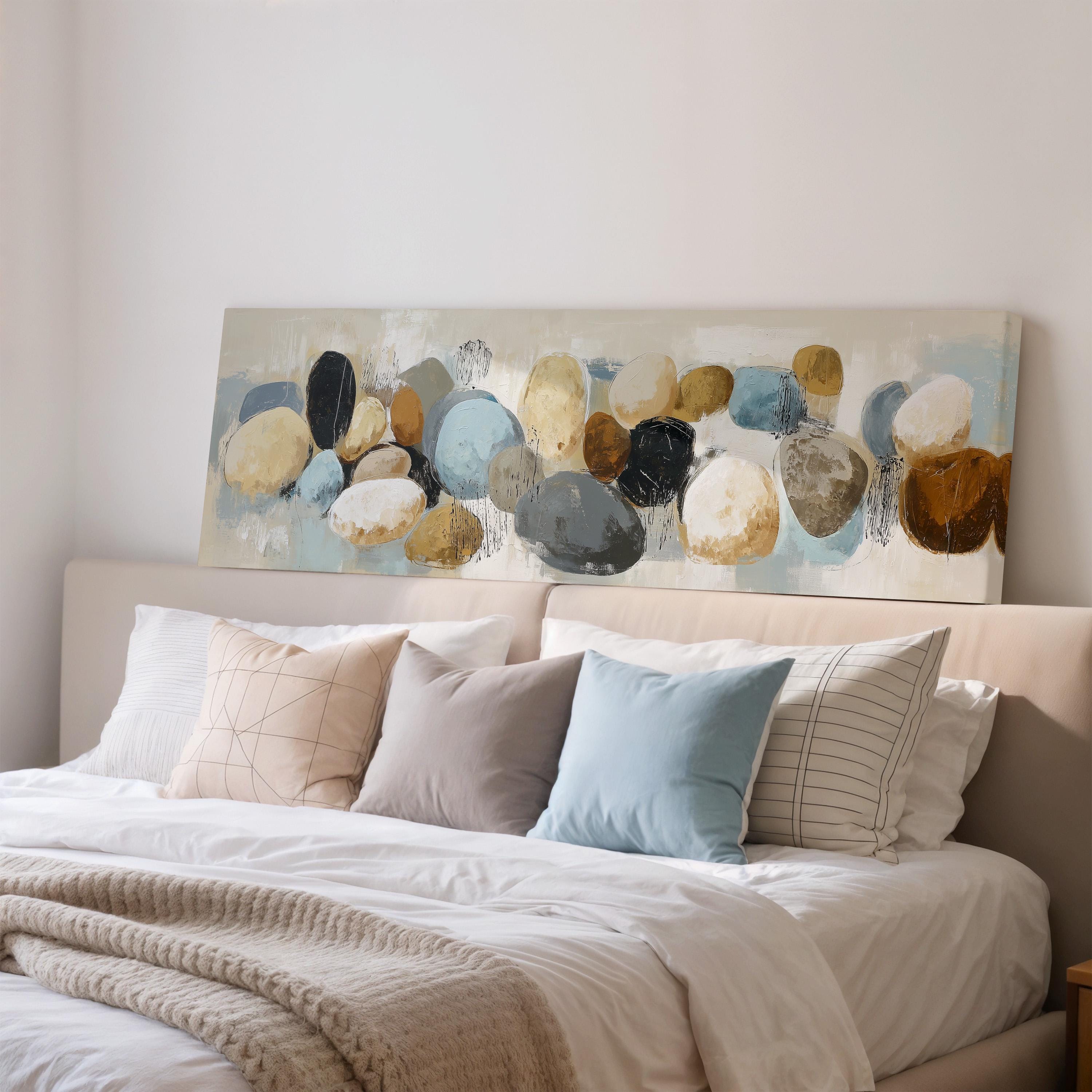 a bedroom with a large bed adorned with white sheets and a variety of colorful pillows. Above the bed, there is a painting of rocks in different shades of blue, gray, and brown.