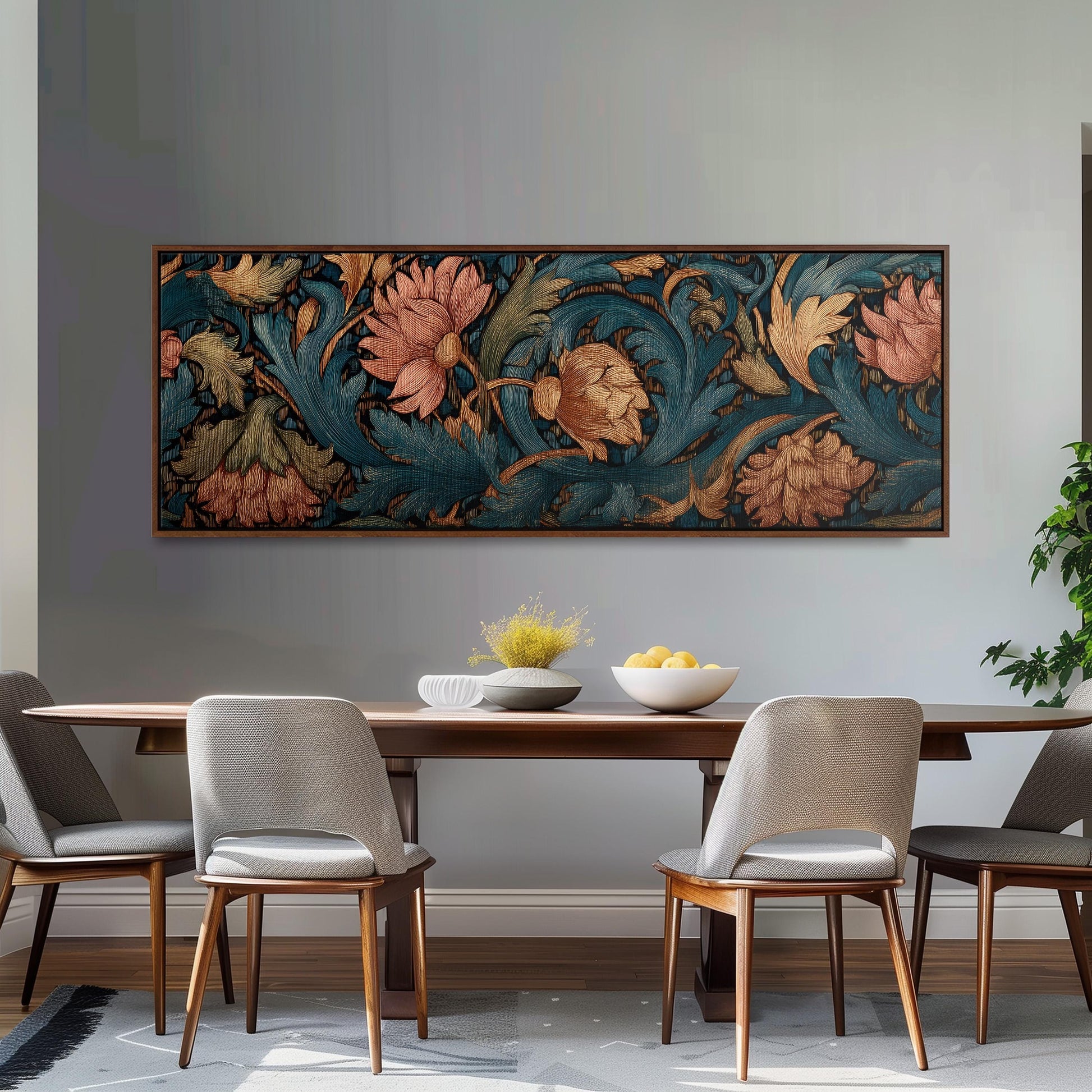 a dining room with a wooden table and four chairs. Above the table, there is a large framed painting depicting a floral design in shades of blue, green, and orange. The painting is hanging on a gray wall. On the table, there is a bowl of fruit and a vase of flowers.