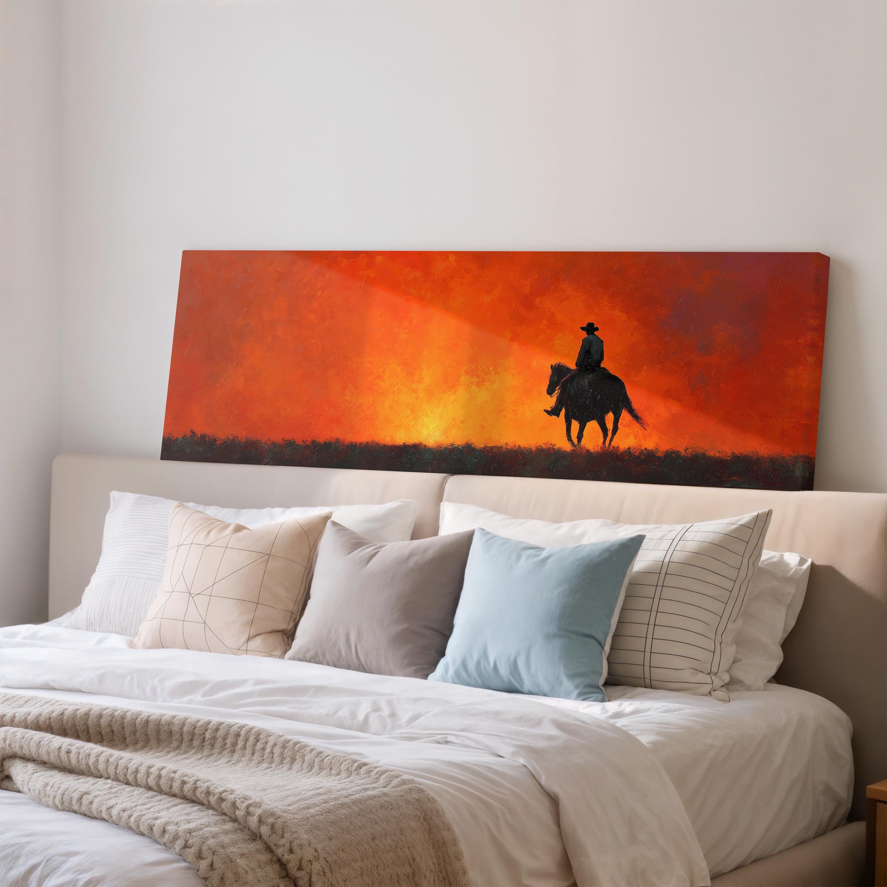 a large painting of a cowboy riding a horse on a sunset-like background, hanging on a wall above a bed with white pillows and a gray blanket.