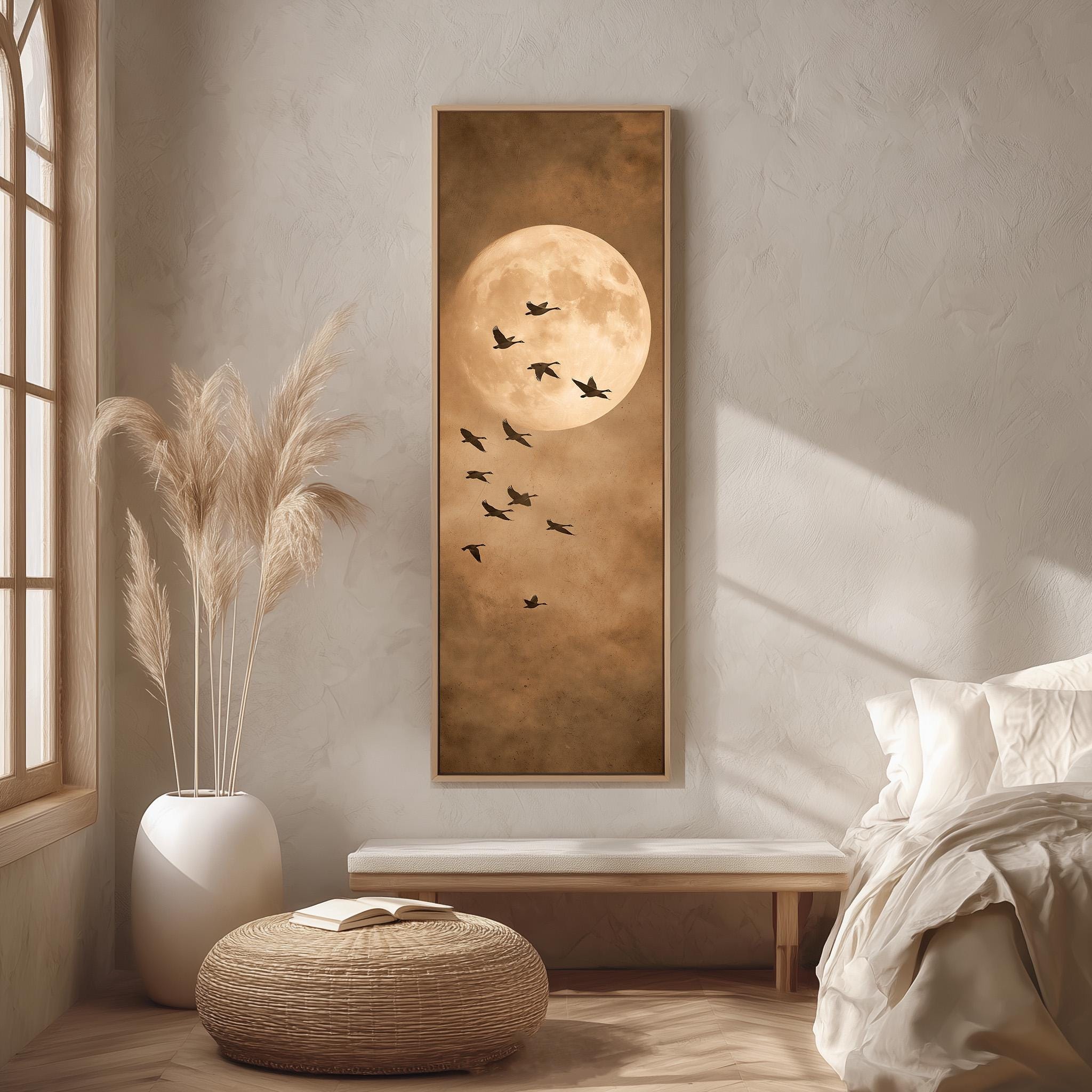 a serene bedroom scene with a large framed picture of a full moon and birds flying in the sky, a white bed with a white pillow, a white vase with tall potted plants, and a woven ottoman.