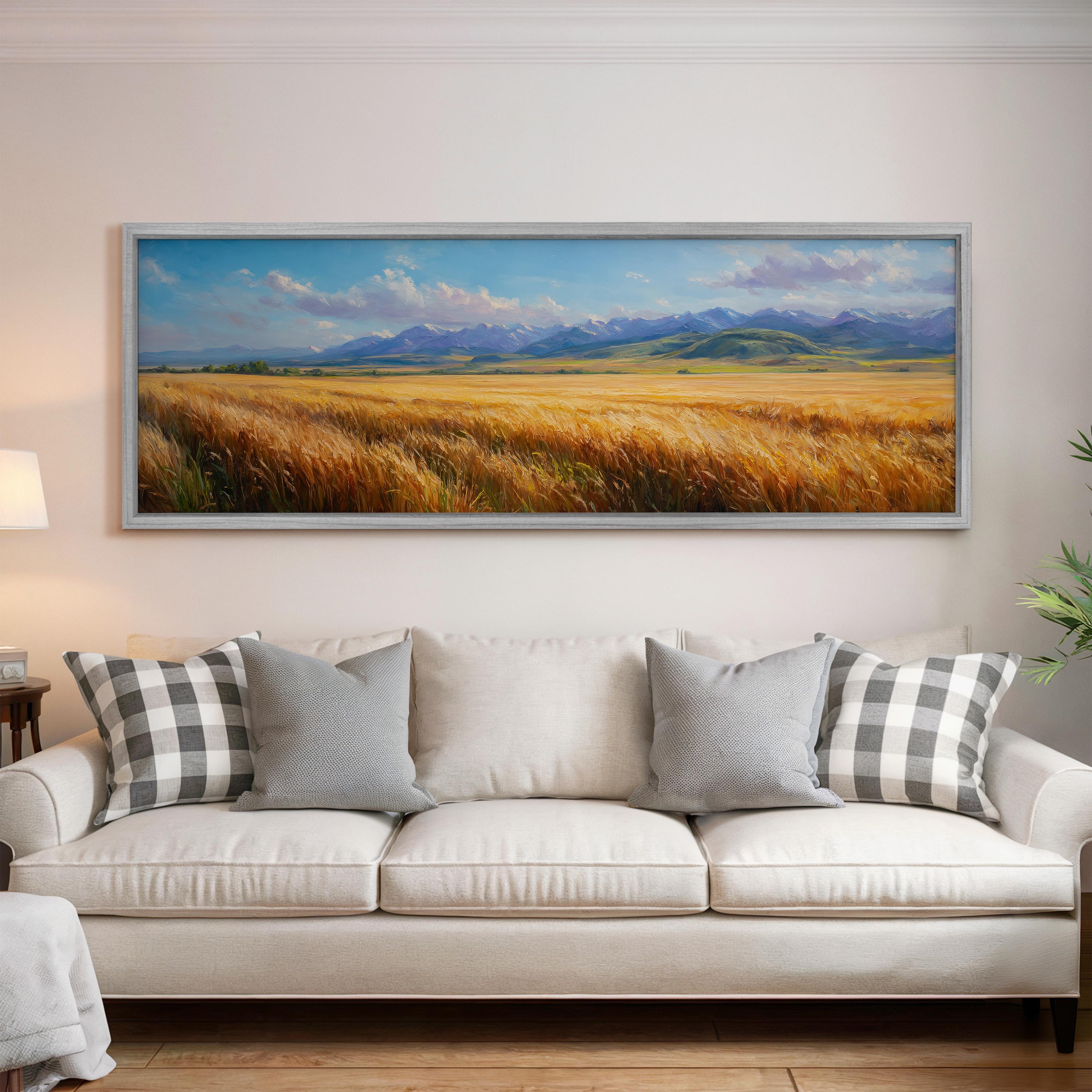 a large, framed painting of a field with mountains in the background, hanging on a wall above a white couch with gray and white patterned pillows.
