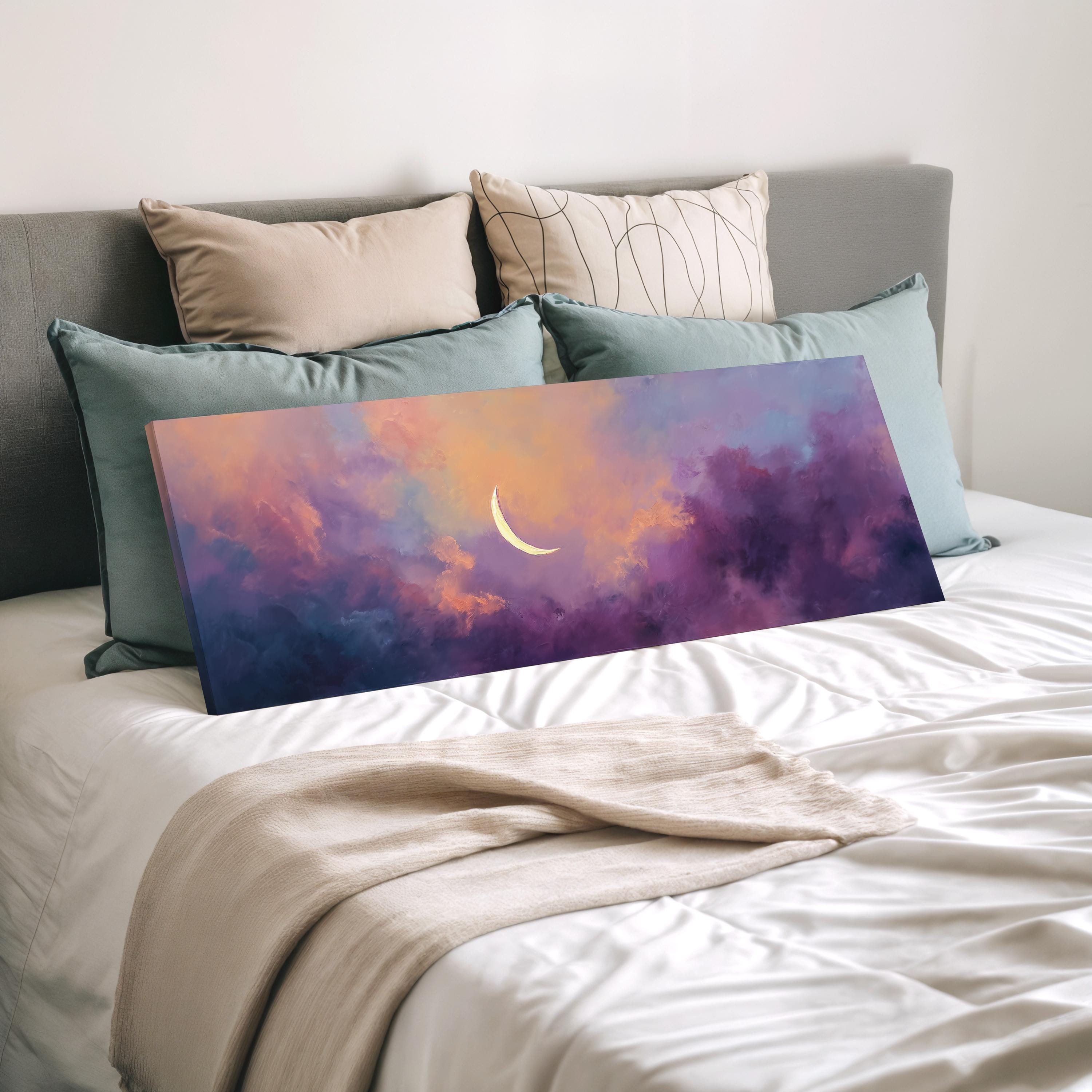a large canvas print of a colorful sunset landscape, with a crescent moon in the sky, placed on a bed with white sheets and pillows.