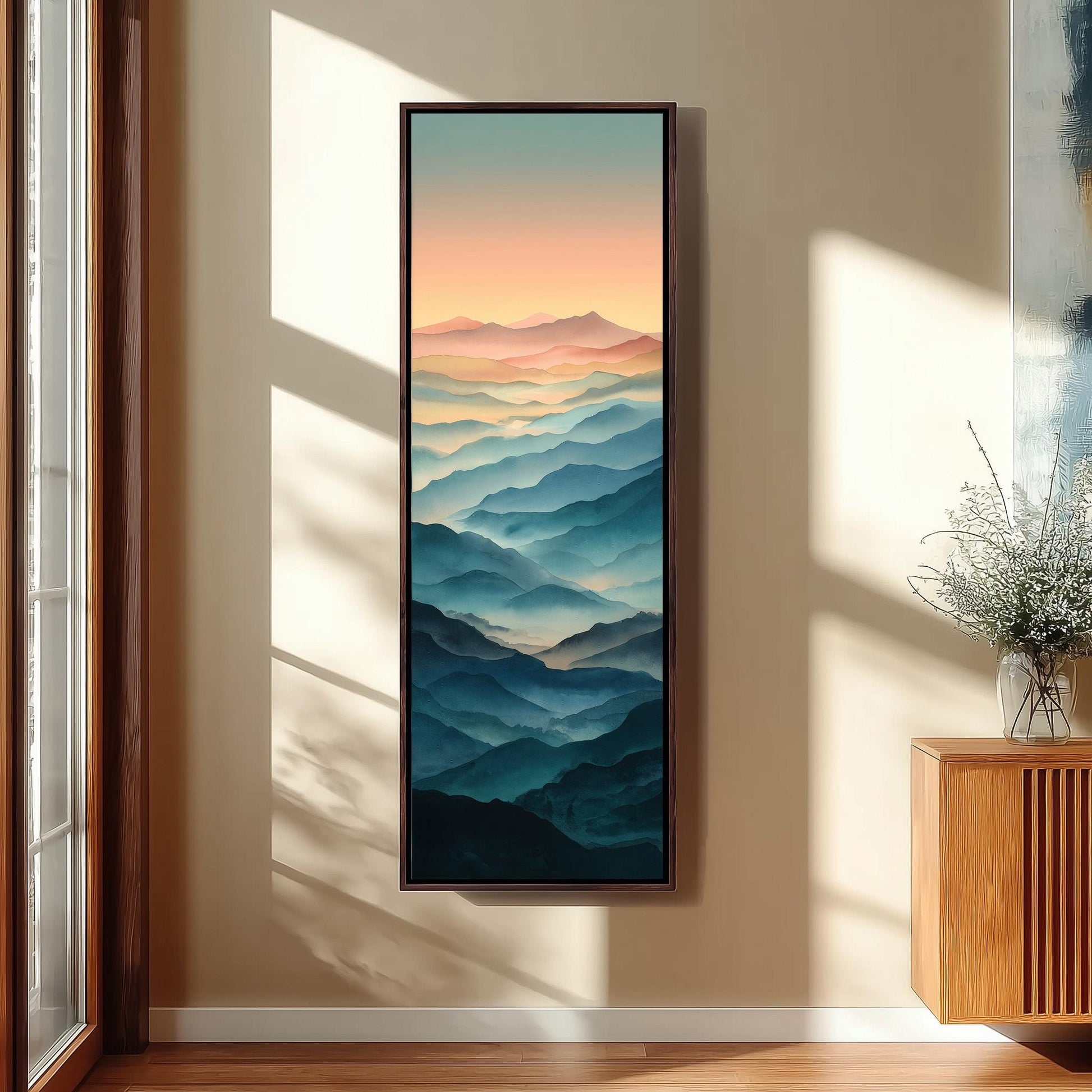 a large, framed painting of a mountain landscape hanging on a wall. The painting depicts a stunning view of mountains with a gradient of colors, creating a sense of depth and distance. The painting is positioned next to a window, allowing natural light to illuminate the artwork and enhance its visual appeal.