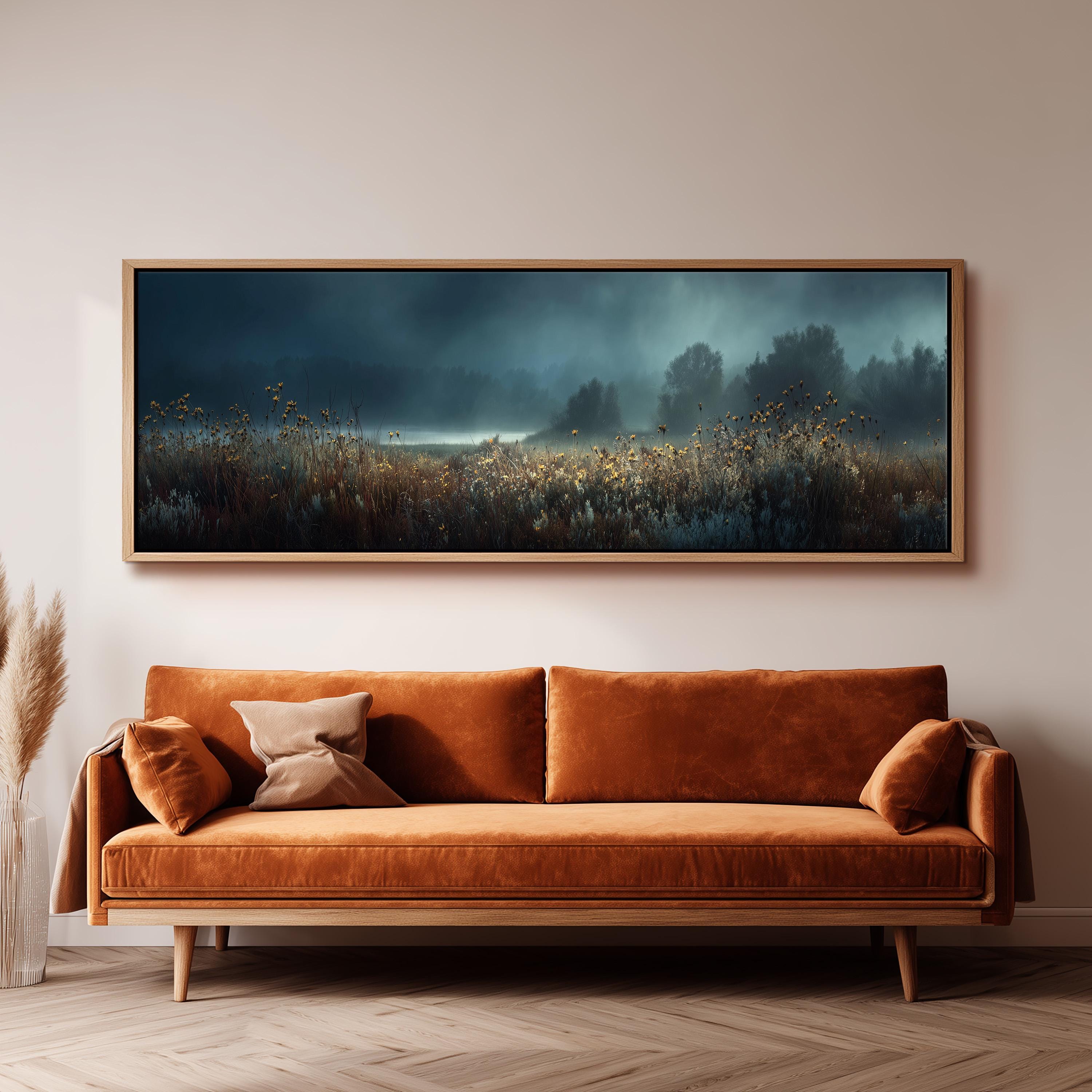 a large, framed painting of a field with a misty, atmospheric background hanging on a wall above a brown sofa.