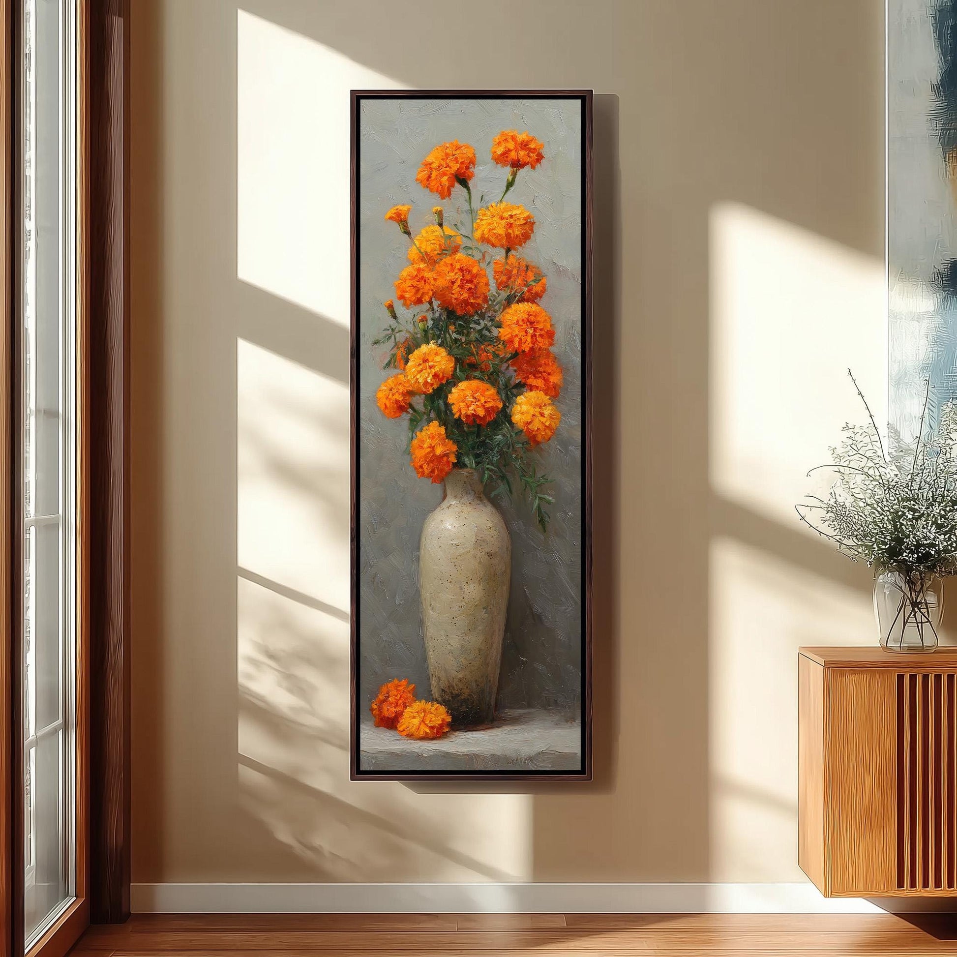 A framed painting of a vase filled with vibrant orange flowers is displayed on a wall in a room with a wooden cabinet and a window.