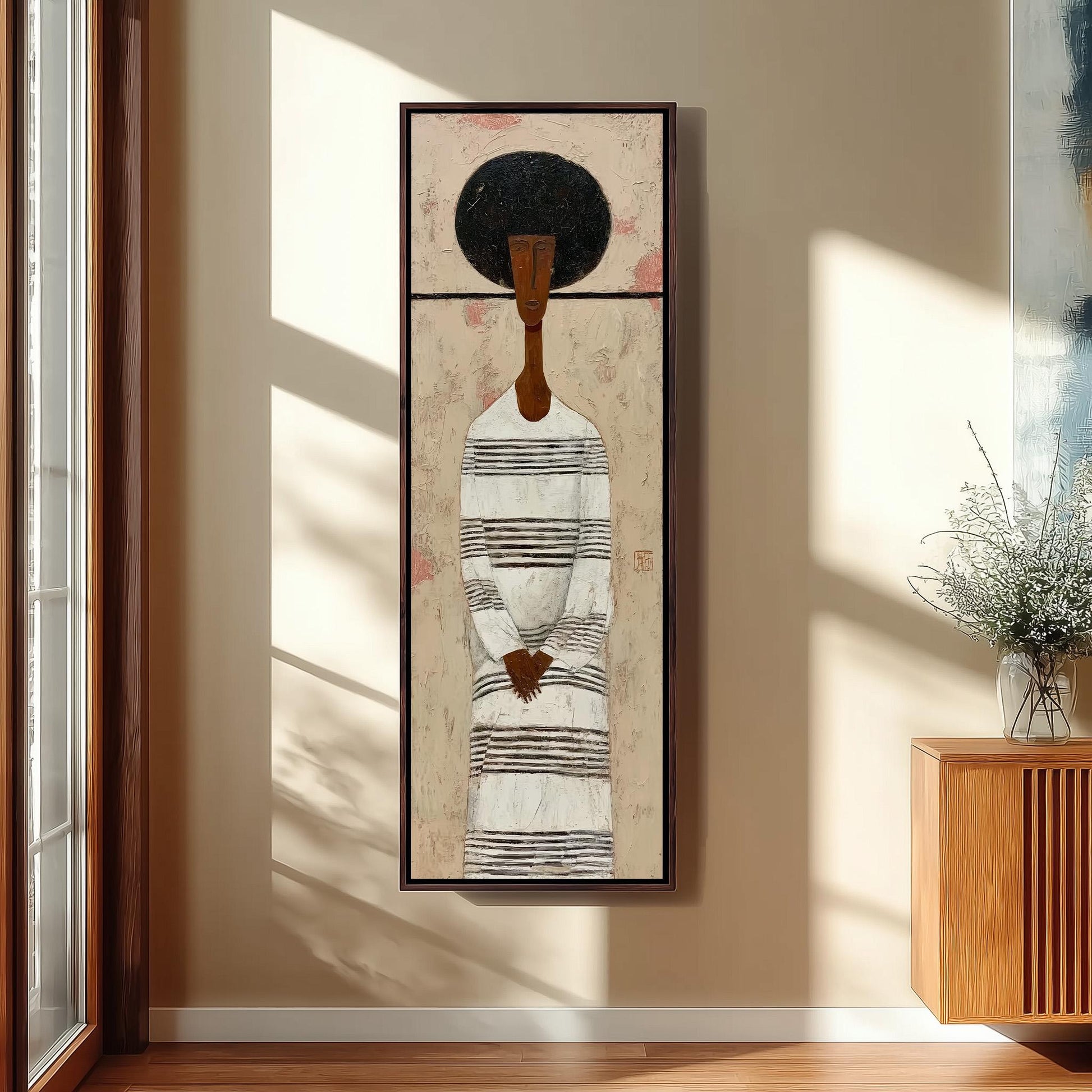 a framed painting of a woman with a black afro hairstyle, wearing a striped dress, hanging on a wall in a room with a wooden cabinet and a vase of flowers.