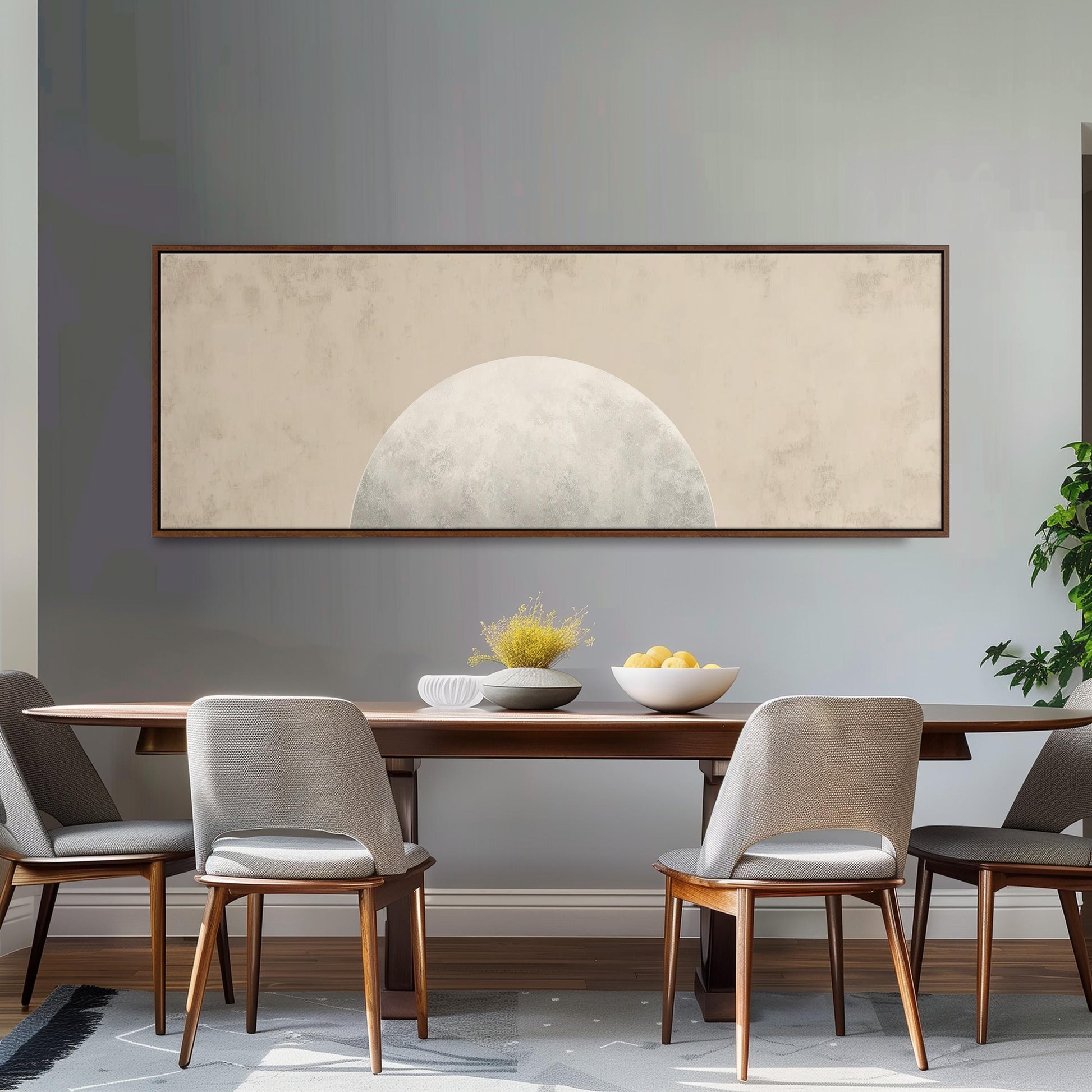 a dining room with a wooden table and four chairs, a large framed artwork hanging on the wall above the table, and a bowl of fruit on the table.