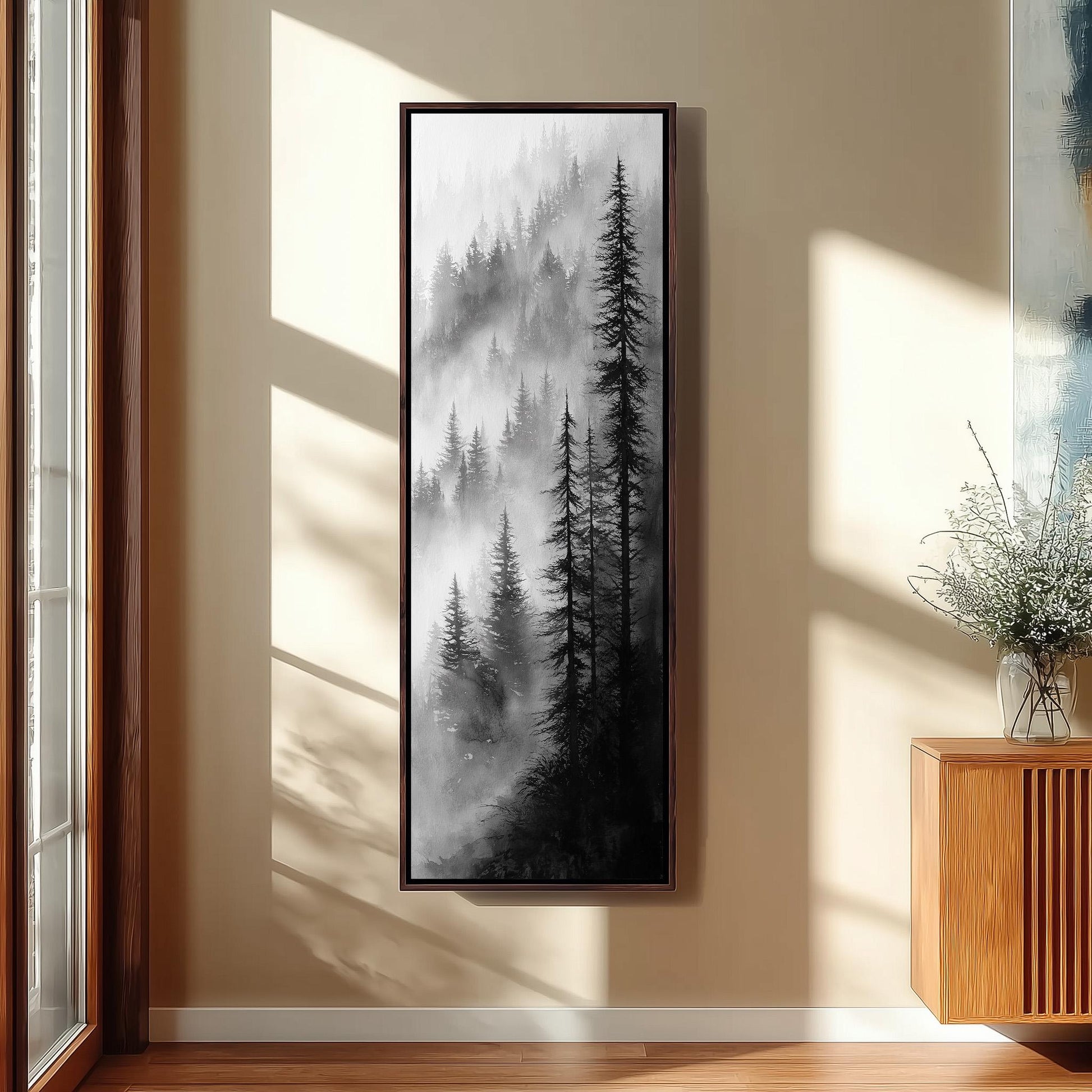 a large black and white painting of a forest scene hanging on a wall in a room with a wooden floor and a window.