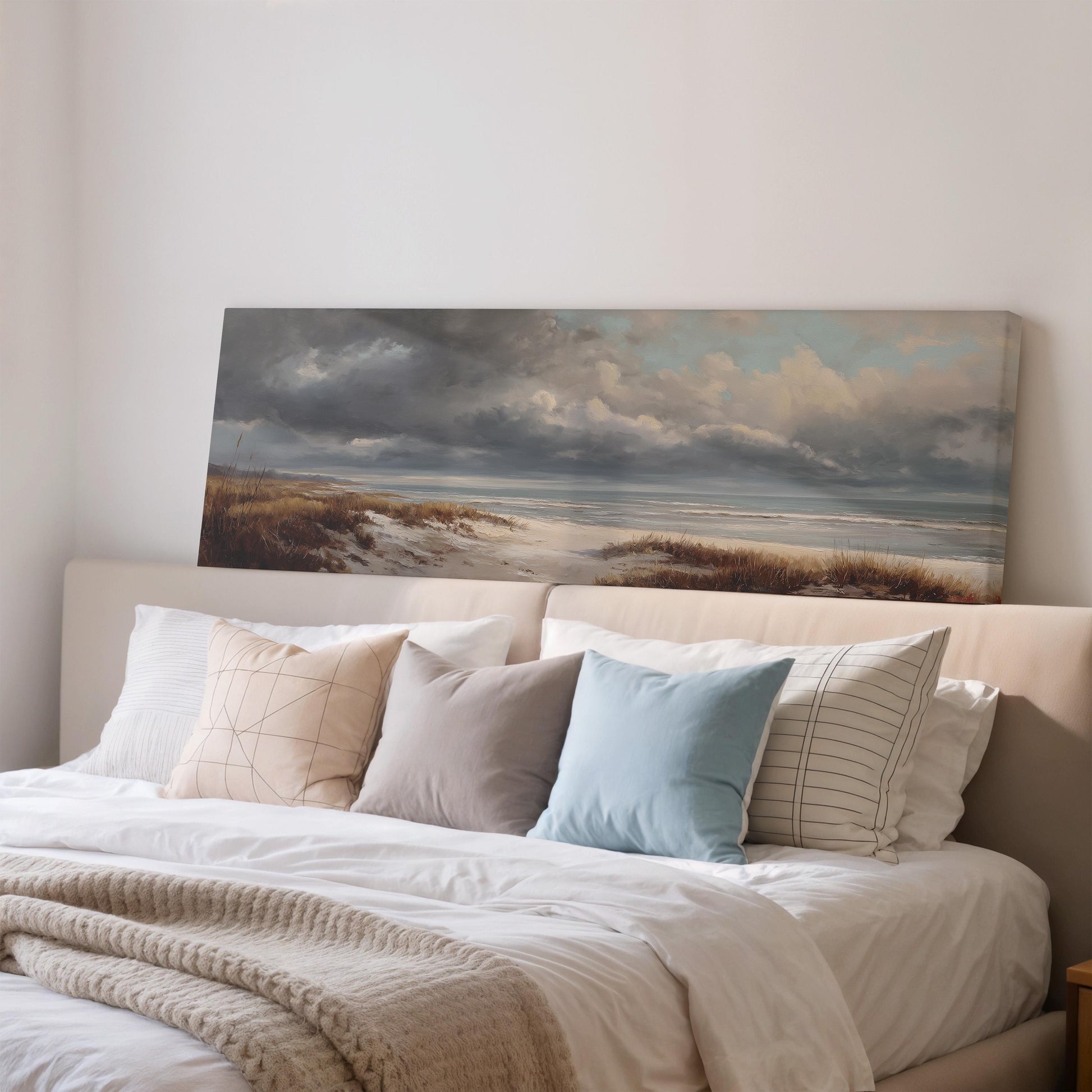 a large painting of a beach scene hanging above a bed with white bedding and various pillows.