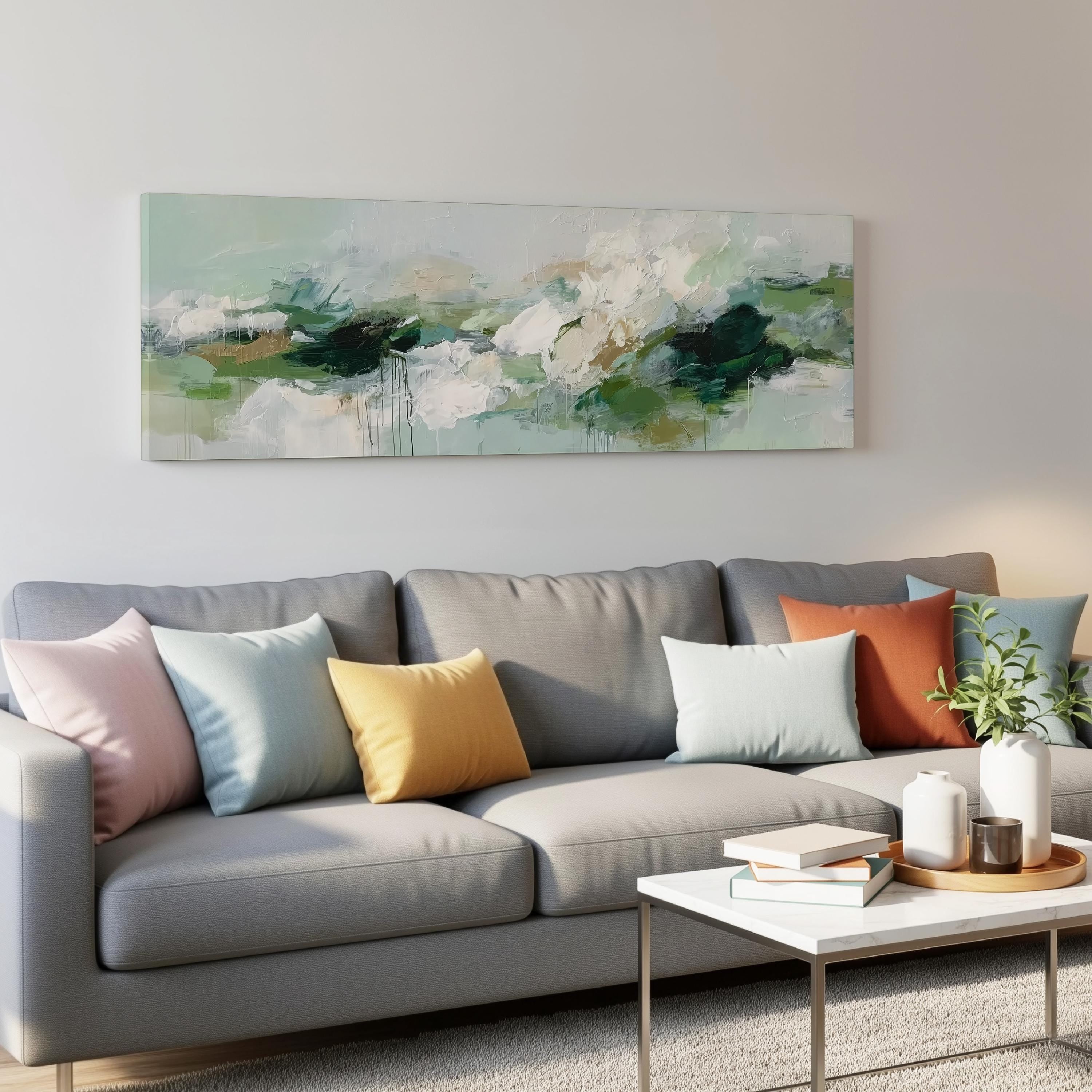 a modern living room with a gray sofa adorned with colorful throw pillows. Above the sofa, there is a large abstract painting hanging on the wall. In front of the sofa, there is a white coffee table with a stack of books and a small plant.