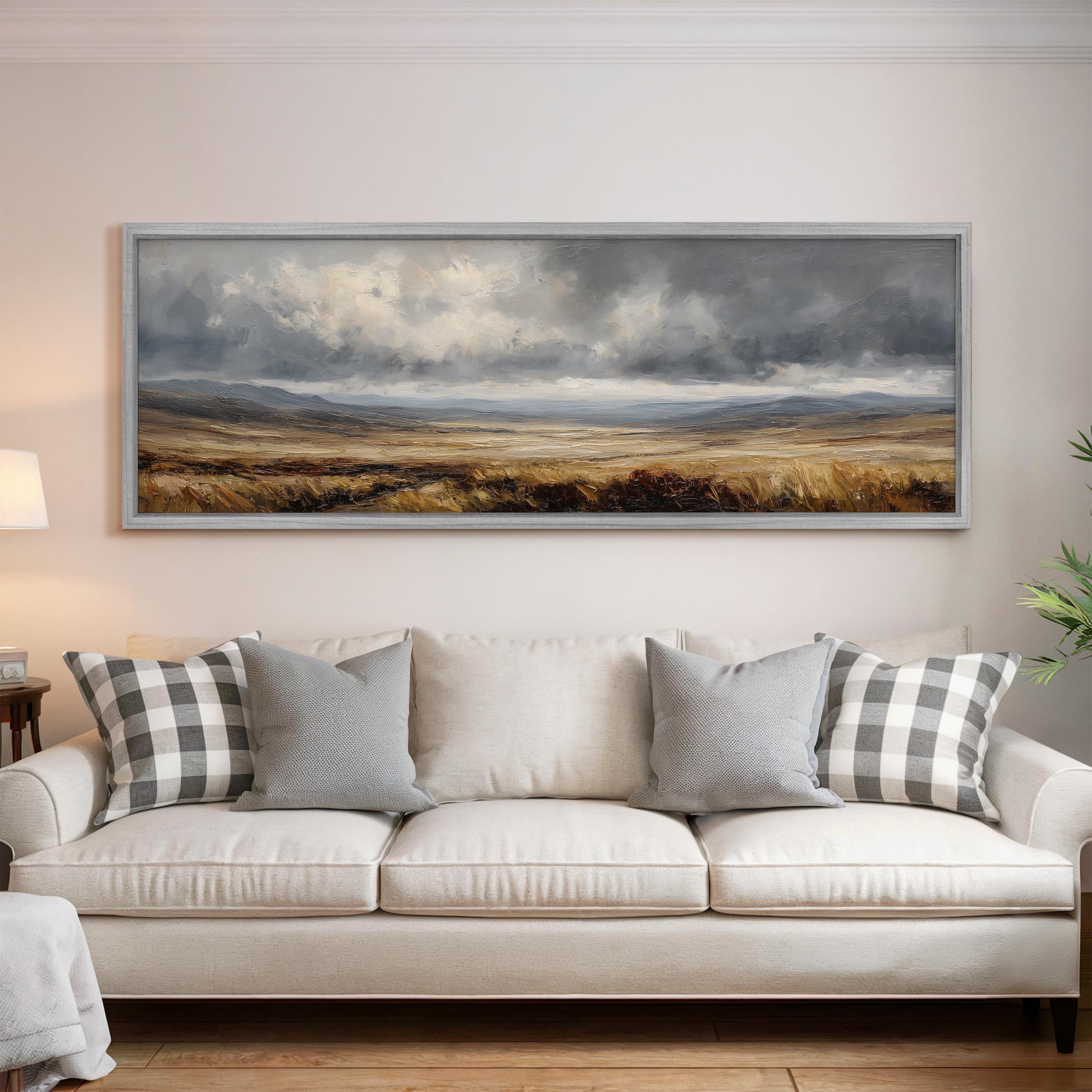 a large landscape painting hanging on a wall above a white sofa with gray and white plaid throw pillows.
