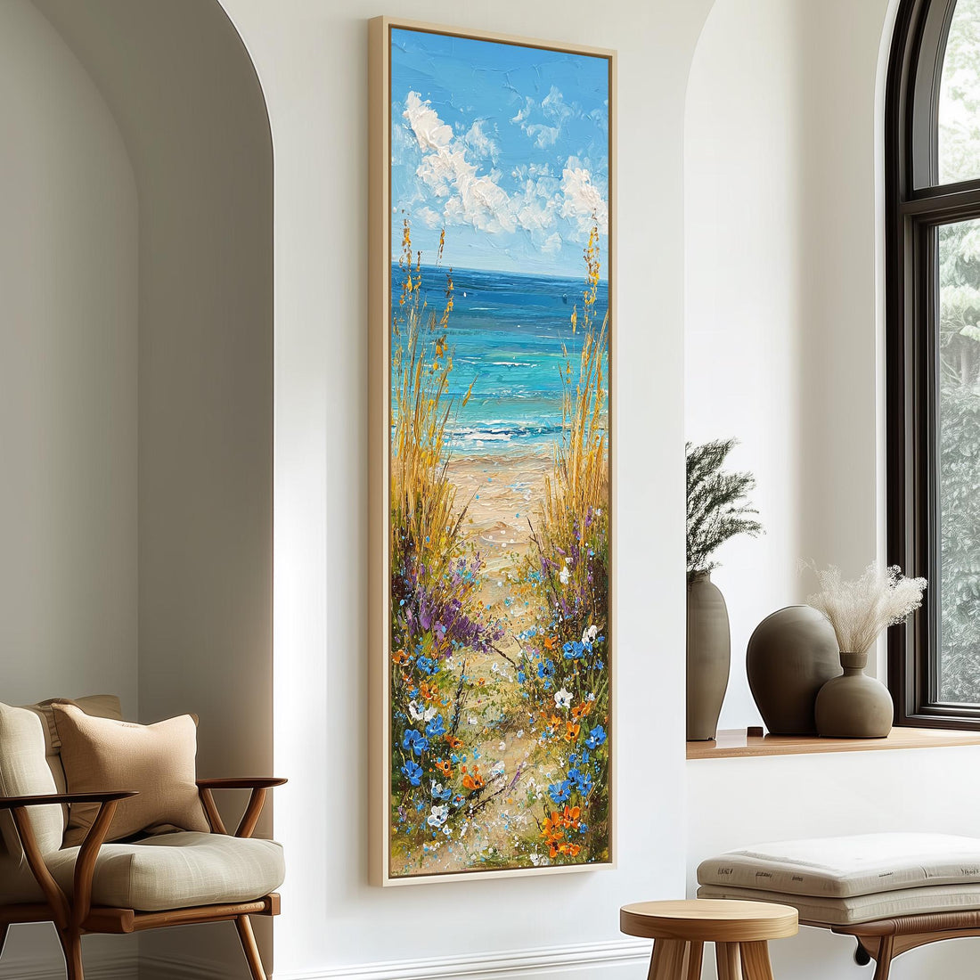 a large painting of a beach scene with a path leading to the ocean, surrounded by tall grass and flowers. The painting is hung on a white wall, and there are two chairs and a small table in the foreground.