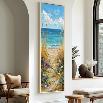 a large painting of a beach scene with a path leading to the ocean, surrounded by tall grass and flowers. The painting is hung on a white wall, and there are two chairs and a small table in the foreground.