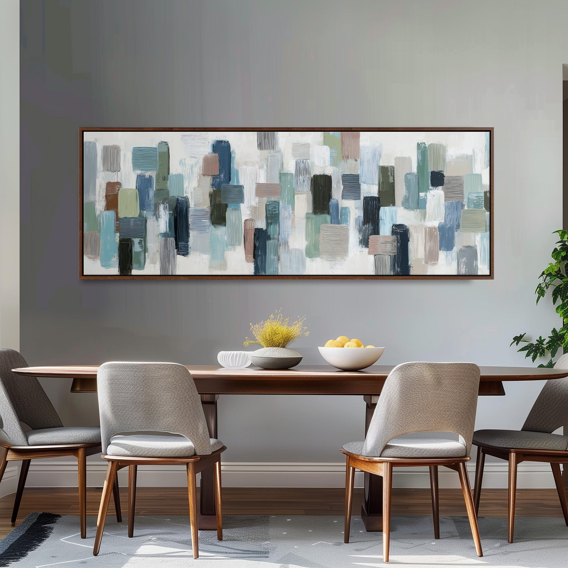 a dining room with a wooden table and four chairs. Above the table, there is a large abstract painting with various shades of blue, green, and gray. The painting is framed and hangs on the wall above the table.