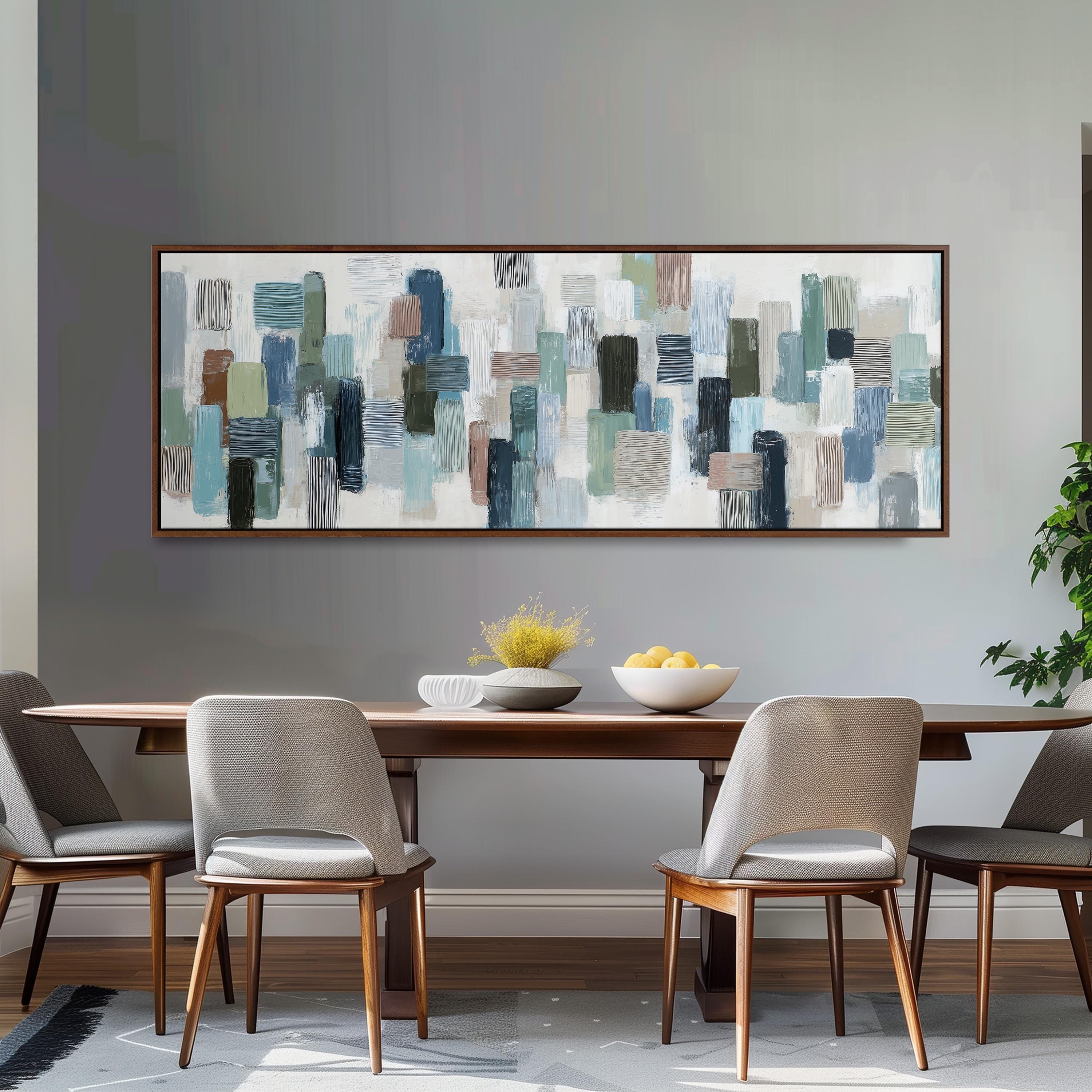 a dining room with a wooden table and four chairs. Above the table, there is a large abstract painting with various shades of blue, green, and gray. The painting is framed and hangs on the wall above the table.