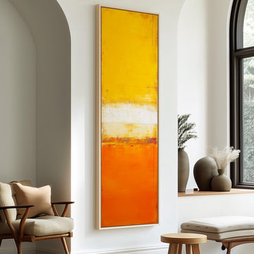 a modern living room with a large abstract painting in warm orange and yellow colors hanging on the wall. The room is furnished with a chair, a table, and a window with a plant on the sill.