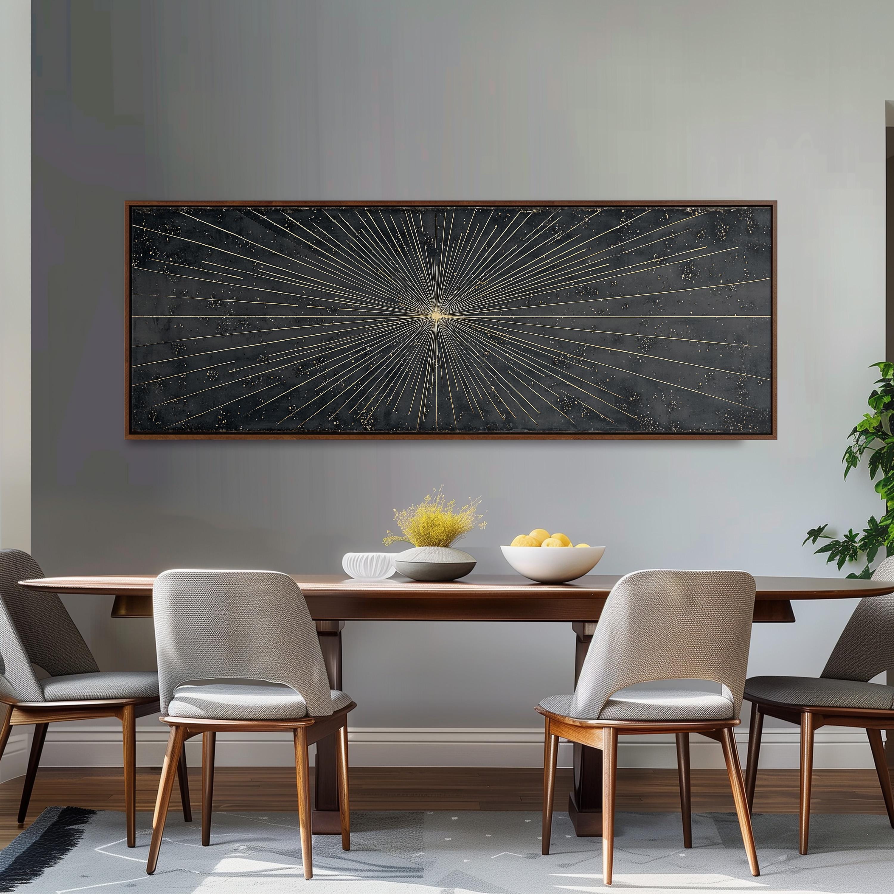 a modern dining room with a wooden table and four upholstered chairs. Above the table, there is a large black and white abstract painting with a central sunburst design. On the table, there is a bowl of fruit and a vase of flowers, adding a touch of color and life to the space.