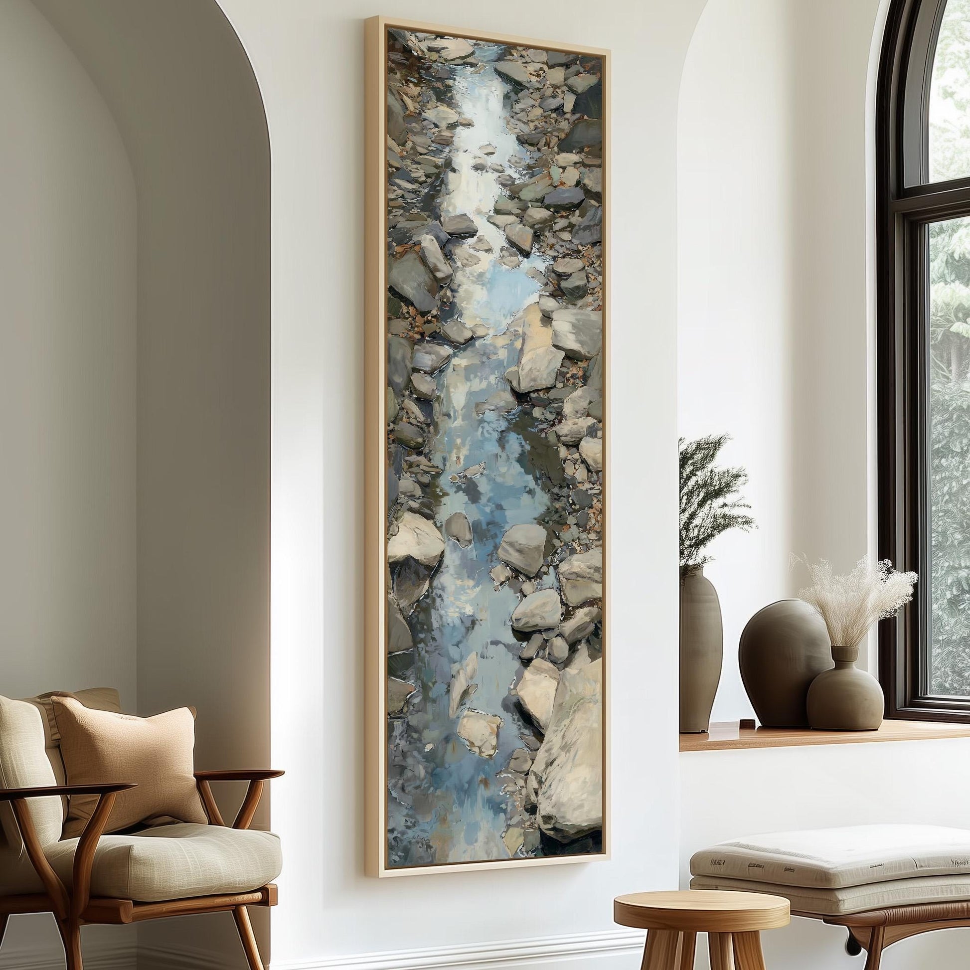 a large painting of a rocky stream flowing through a natural landscape, hanging on a wall in a room with a wooden chair and a small table.
