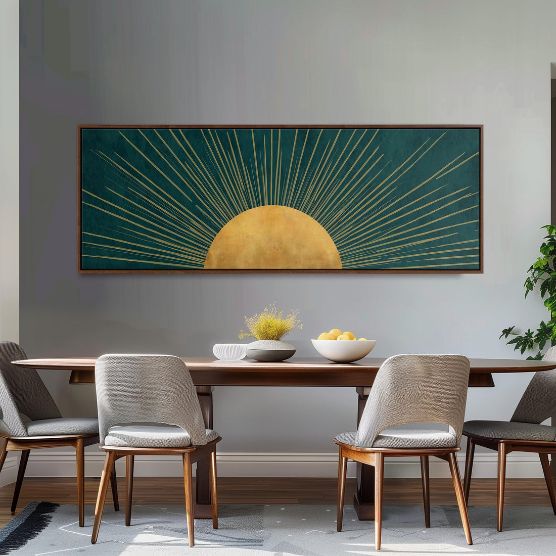 a dining room with a wooden table and four chairs. Above the table, there is a large framed artwork depicting a sun with rays radiating from it. The artwork is set against a gray wall, and the table is adorned with a bowl of fruit and a vase of flowers.