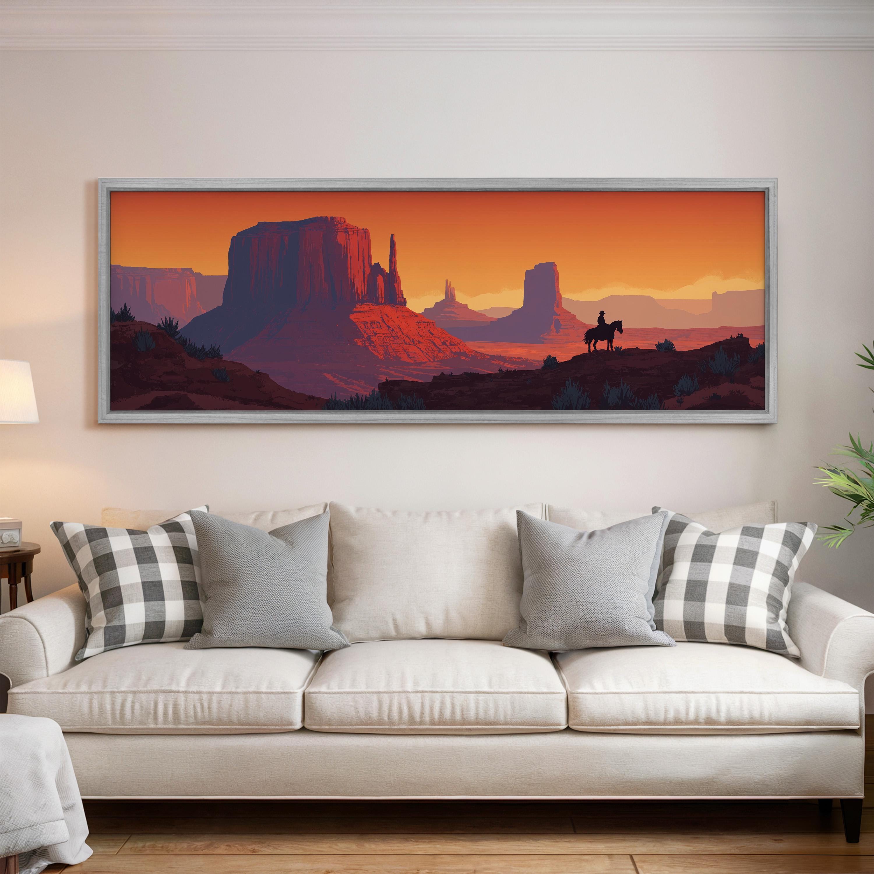 a large framed painting of a desert landscape with mountains and a cowboy on horseback, hanging on a wall above a white couch with patterned throw pillows.