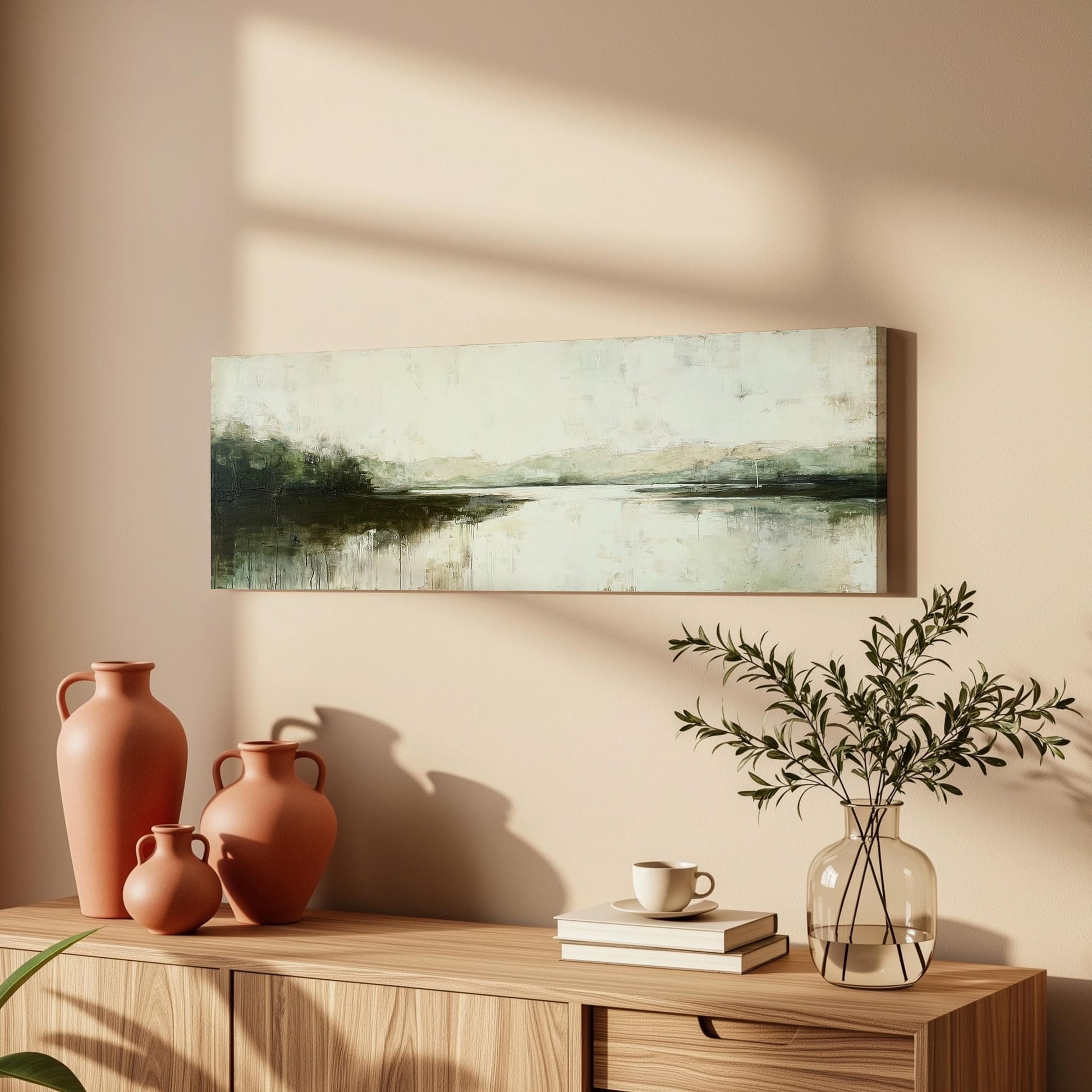 a wooden cabinet with a painting of a landscape hanging on the wall above it. The cabinet also has three orange vases and a glass vase with greenery, as well as a stack of books and a coffee cup on the surface.