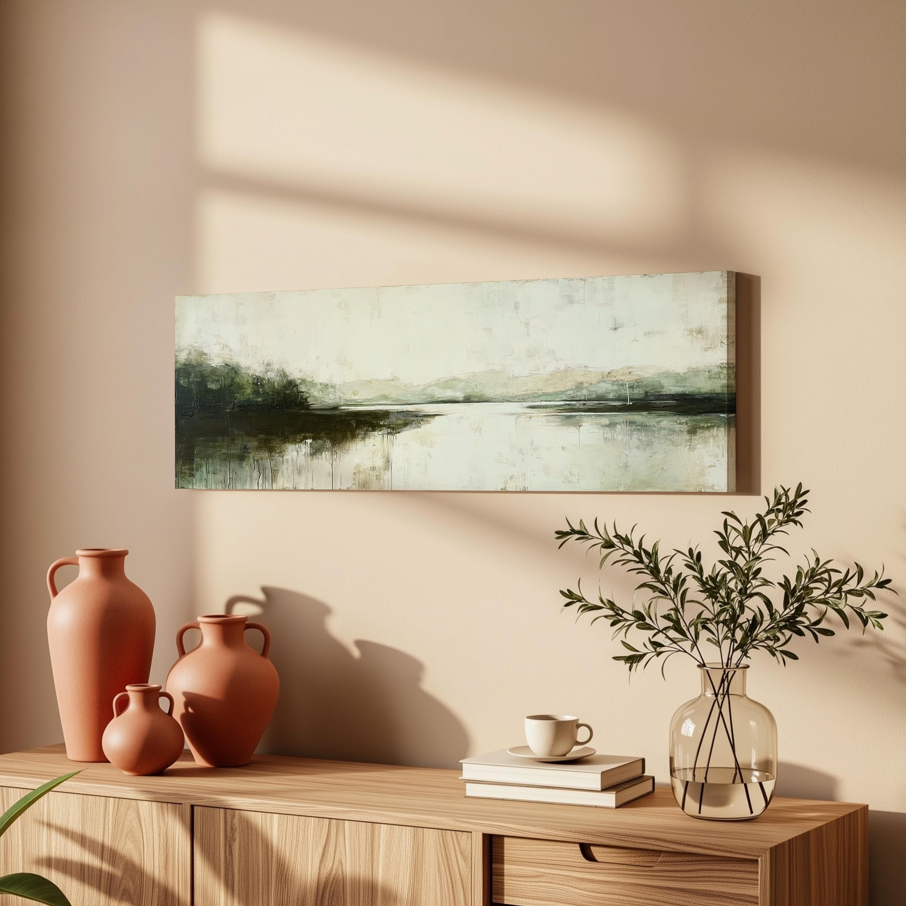 a wooden cabinet with a painting of a landscape hanging on the wall above it. The cabinet also has three orange vases and a glass vase with greenery, as well as a stack of books and a coffee cup on the surface.