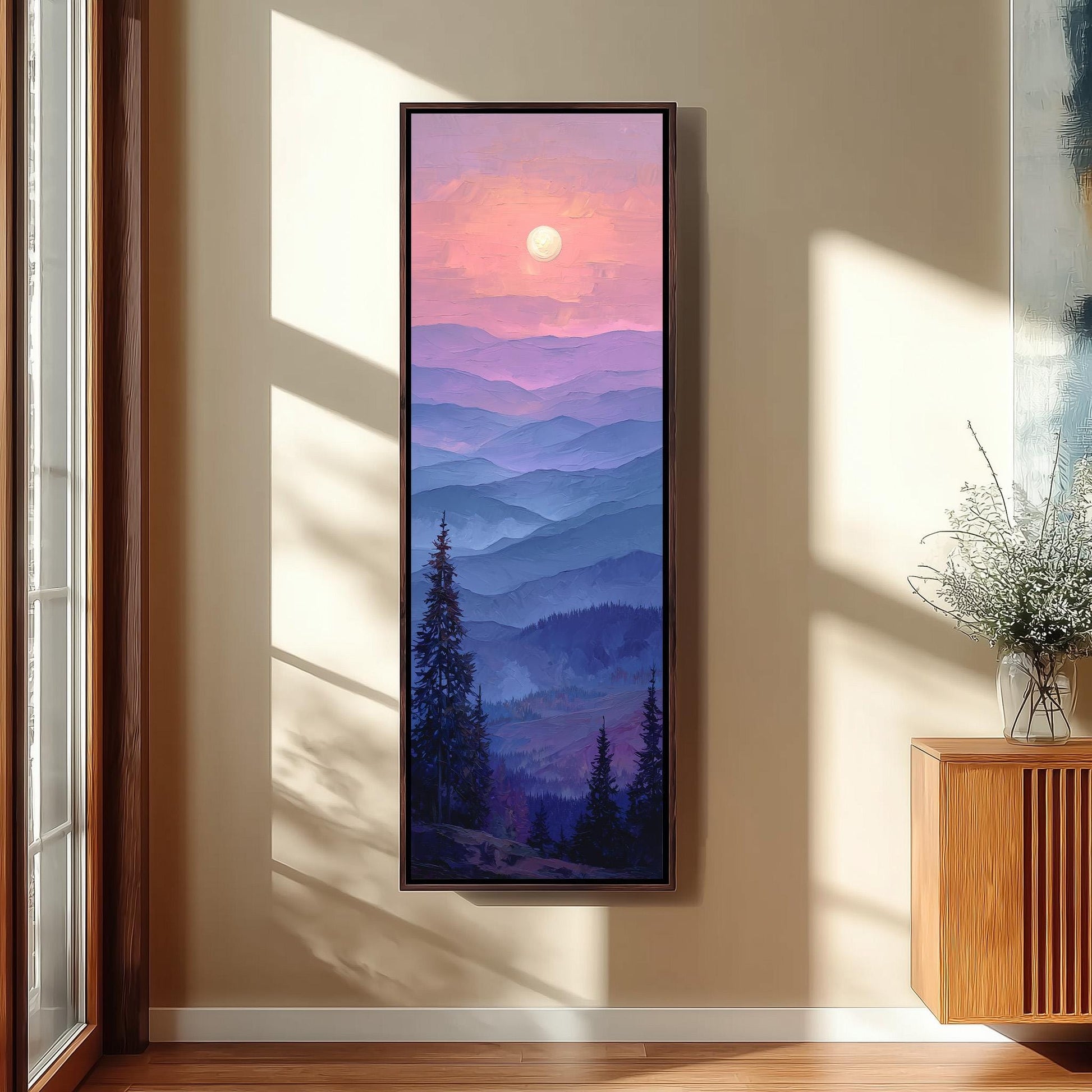 a large framed painting of a mountain landscape with a sunset in the background, hanging on a wall in a room with a wooden floor and a window.