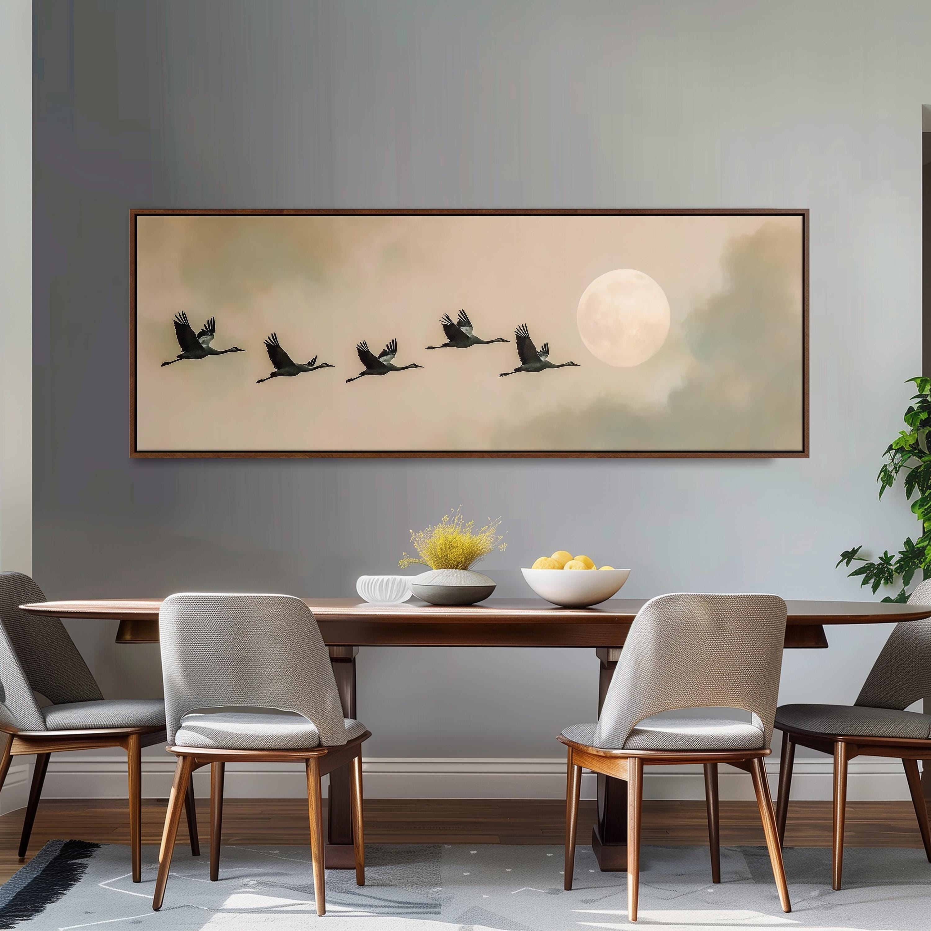 a dining room with a large framed painting of a flock of birds flying across a cloudy sky above a table with a bowl of fruit.