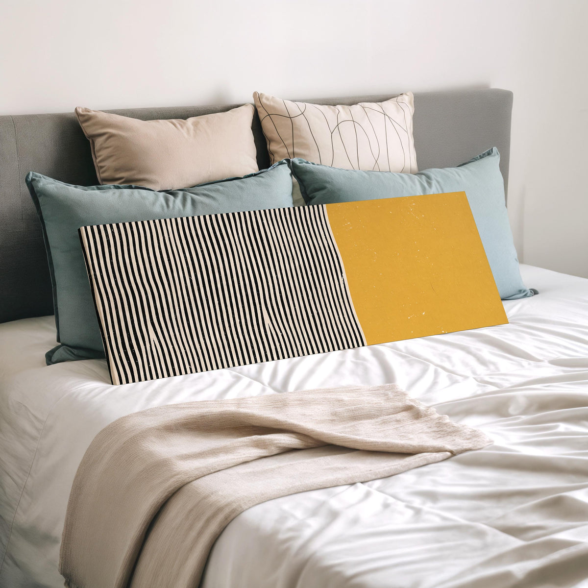 Black wavy stripes beside a mustard block wide panoramic canvas print laid on a bed to show its size