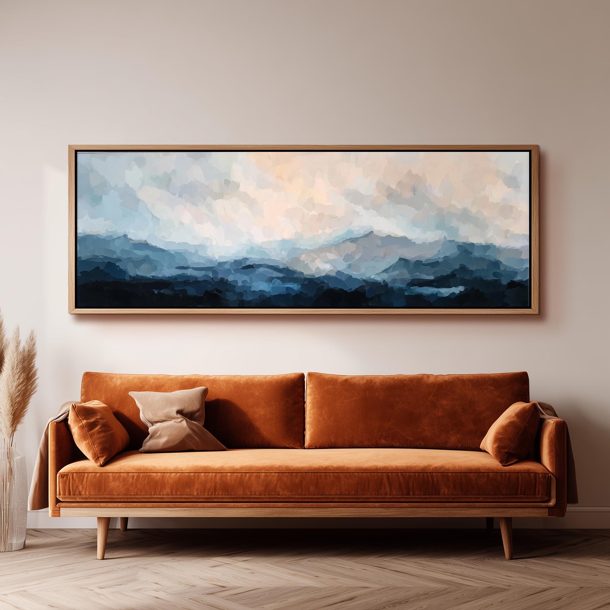 a large, rectangular painting hanging on a wall above a brown sofa with orange cushions.