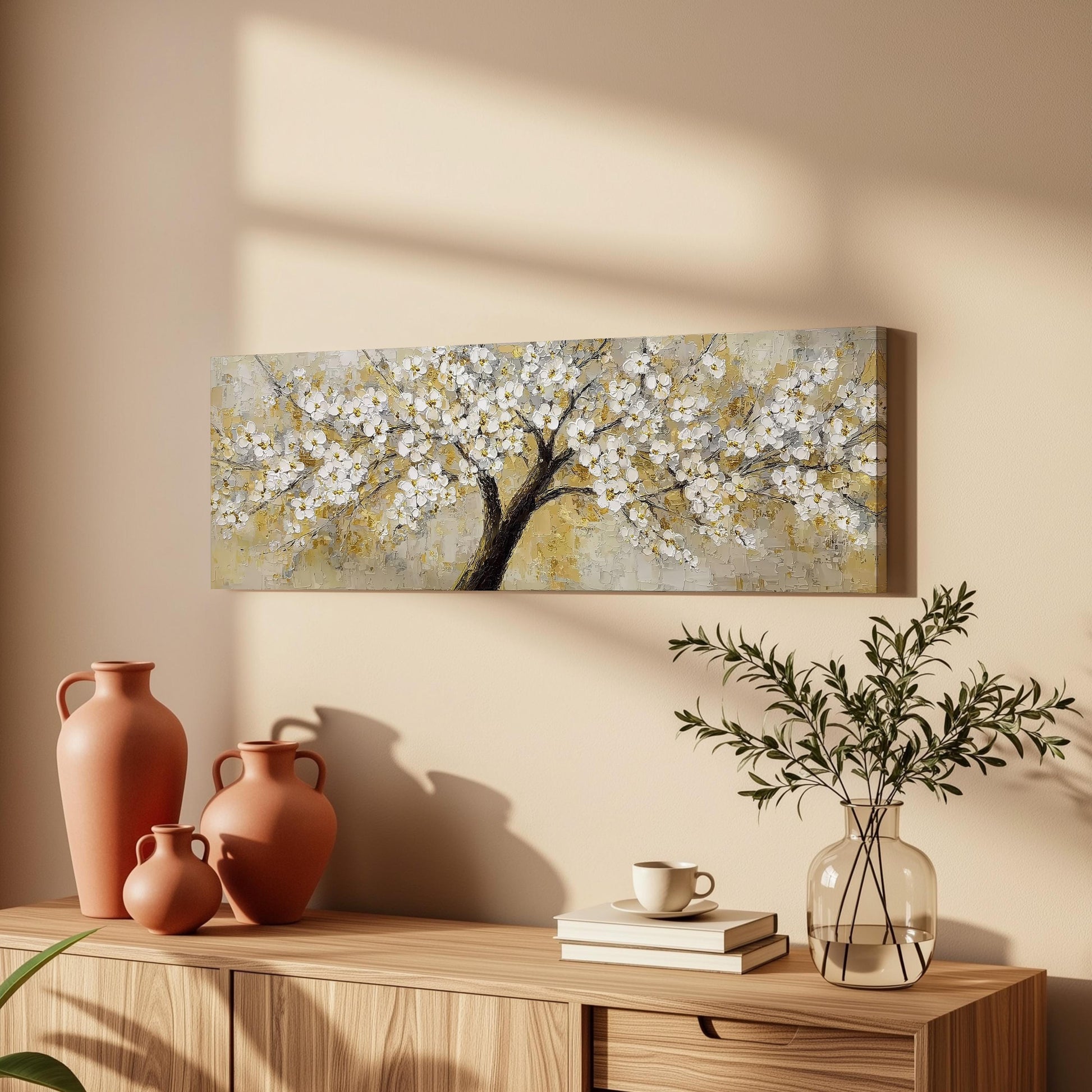 a wooden cabinet with a painting of a tree with white flowers hanging on the wall above it. The cabinet also has three orange vases and a glass vase with greenery on top of it.
