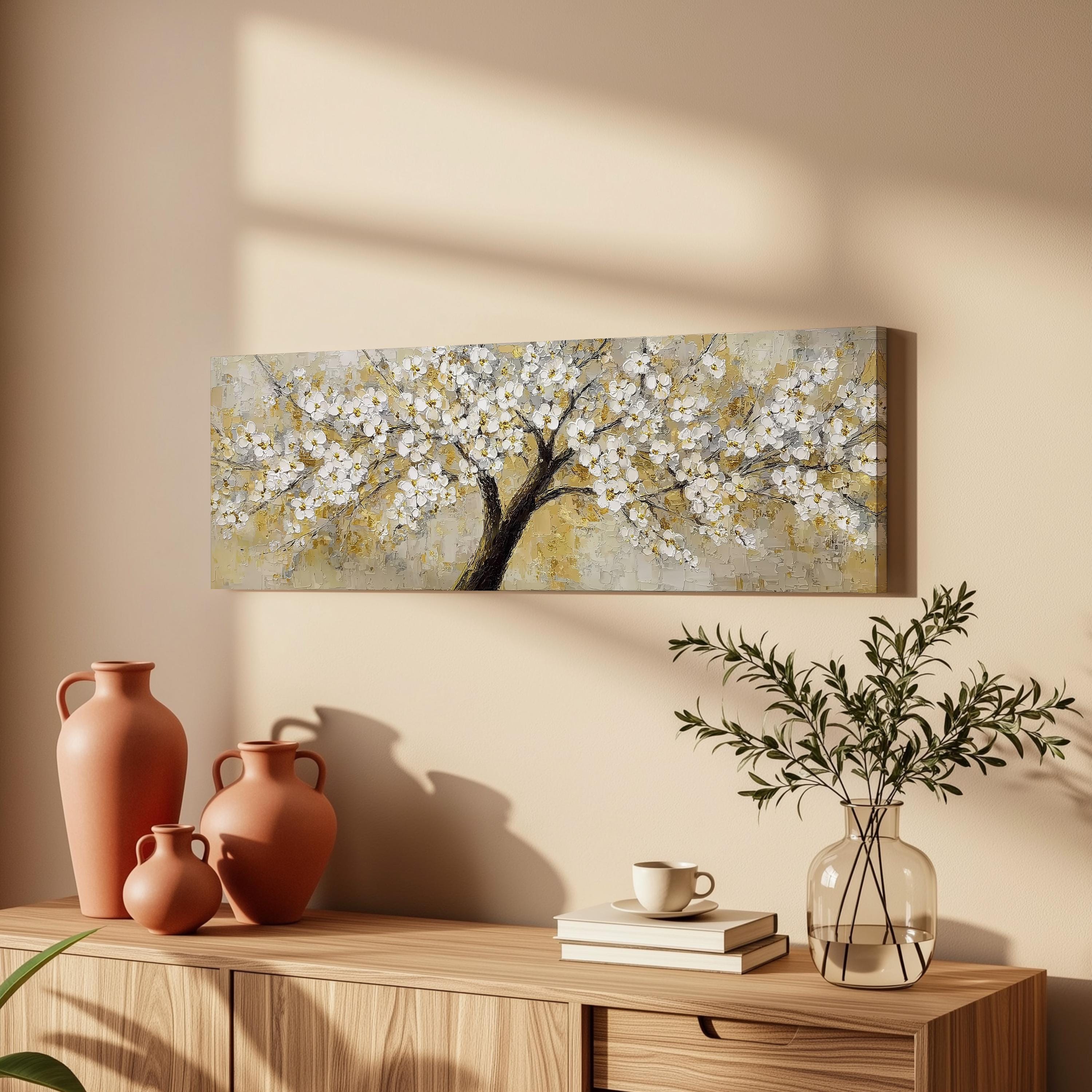 a wooden cabinet with a painting of a tree with white flowers hanging on the wall above it. The cabinet also has three orange vases and a glass vase with greenery on top of it.