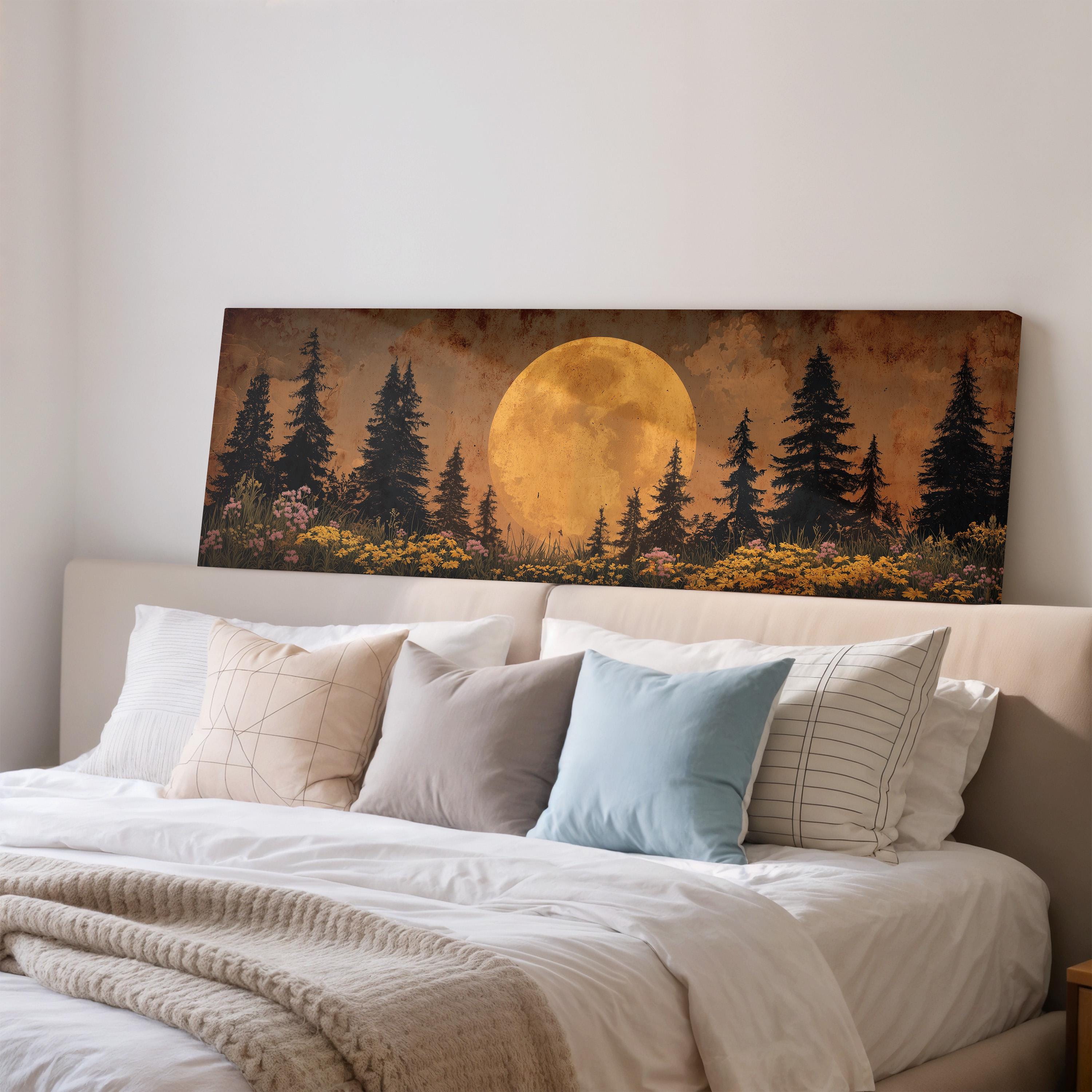 a large painting of a forest scene with a full moon in the background, hanging on a wall above a bed with white pillows and a gray blanket.