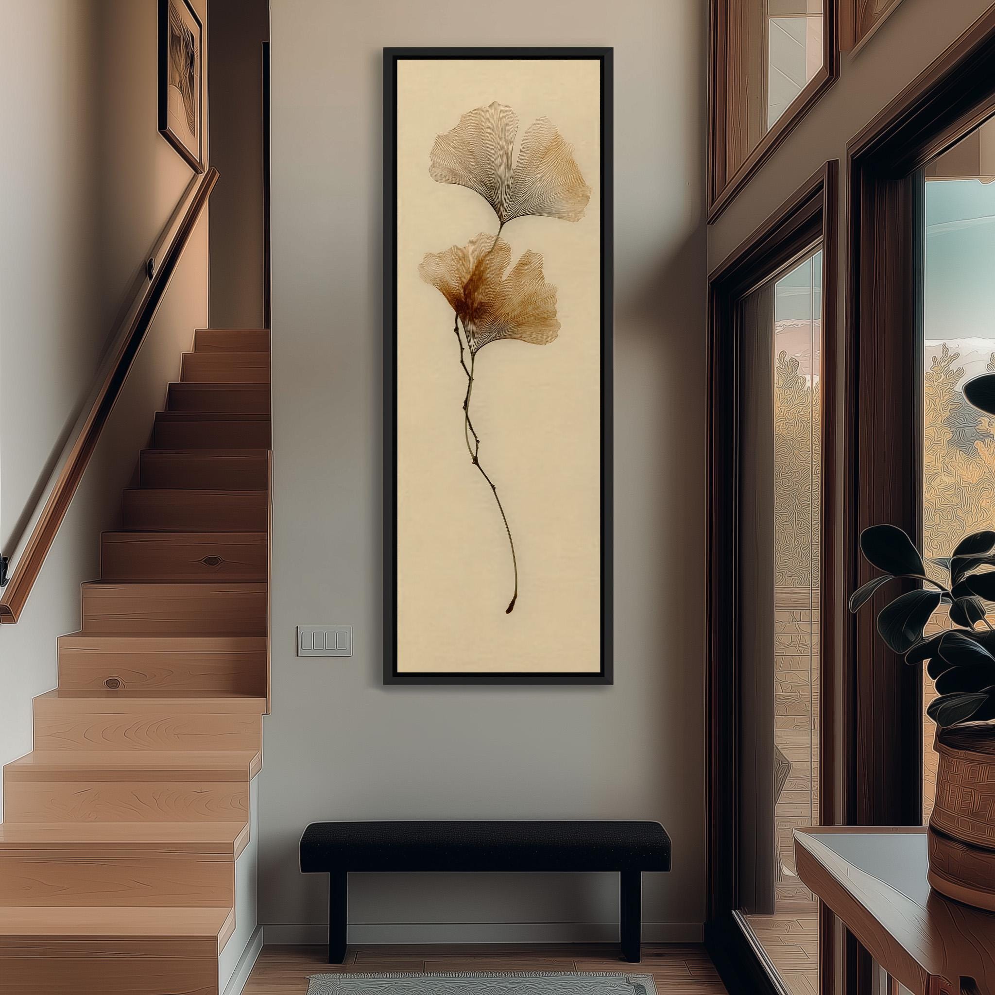 a hallway with a wooden staircase, a large framed artwork of a leaf on the wall, and a black bench in the foreground.