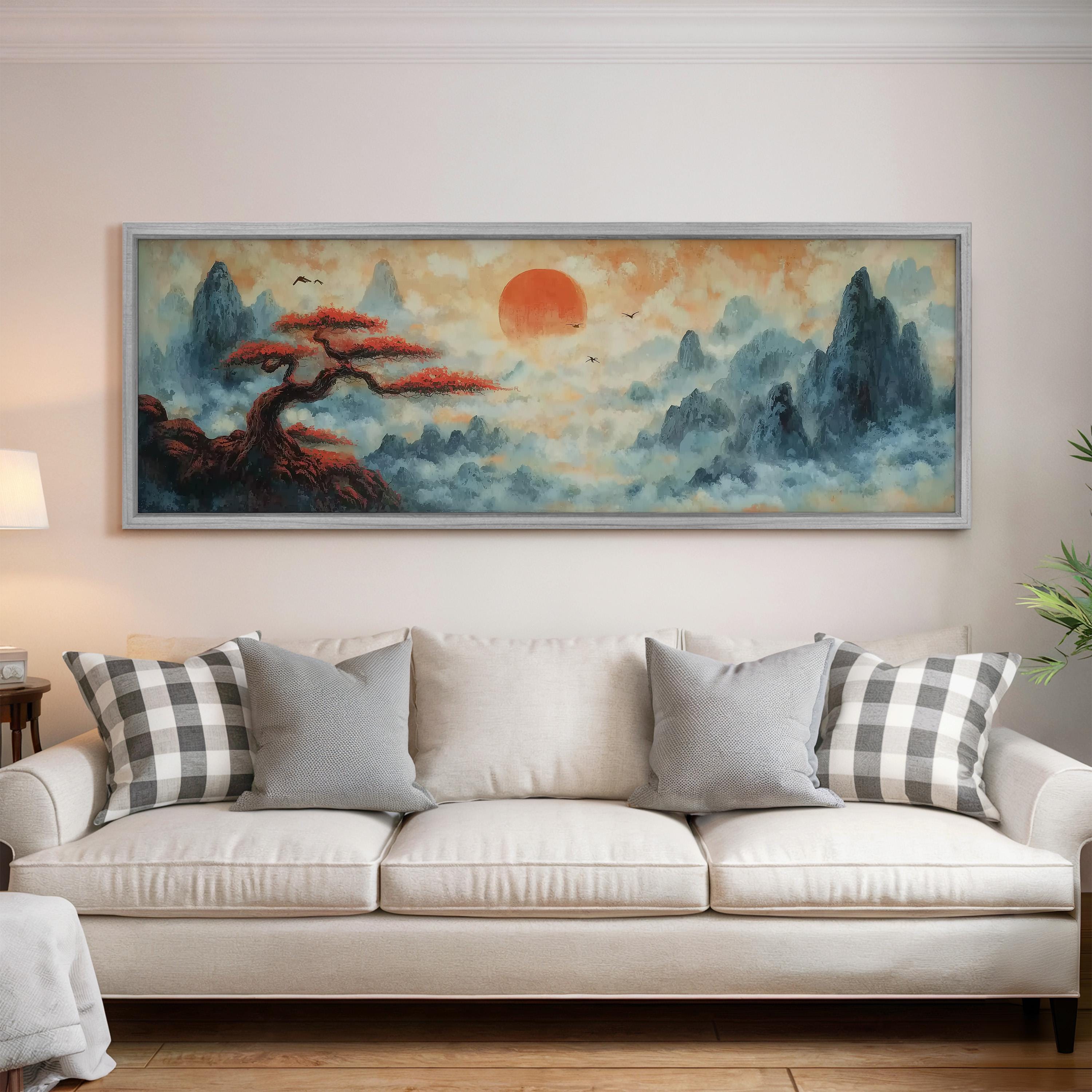 a large painting of a landscape with a tree and mountains, hanging on a wall above a white sofa with gray and white patterned pillows.