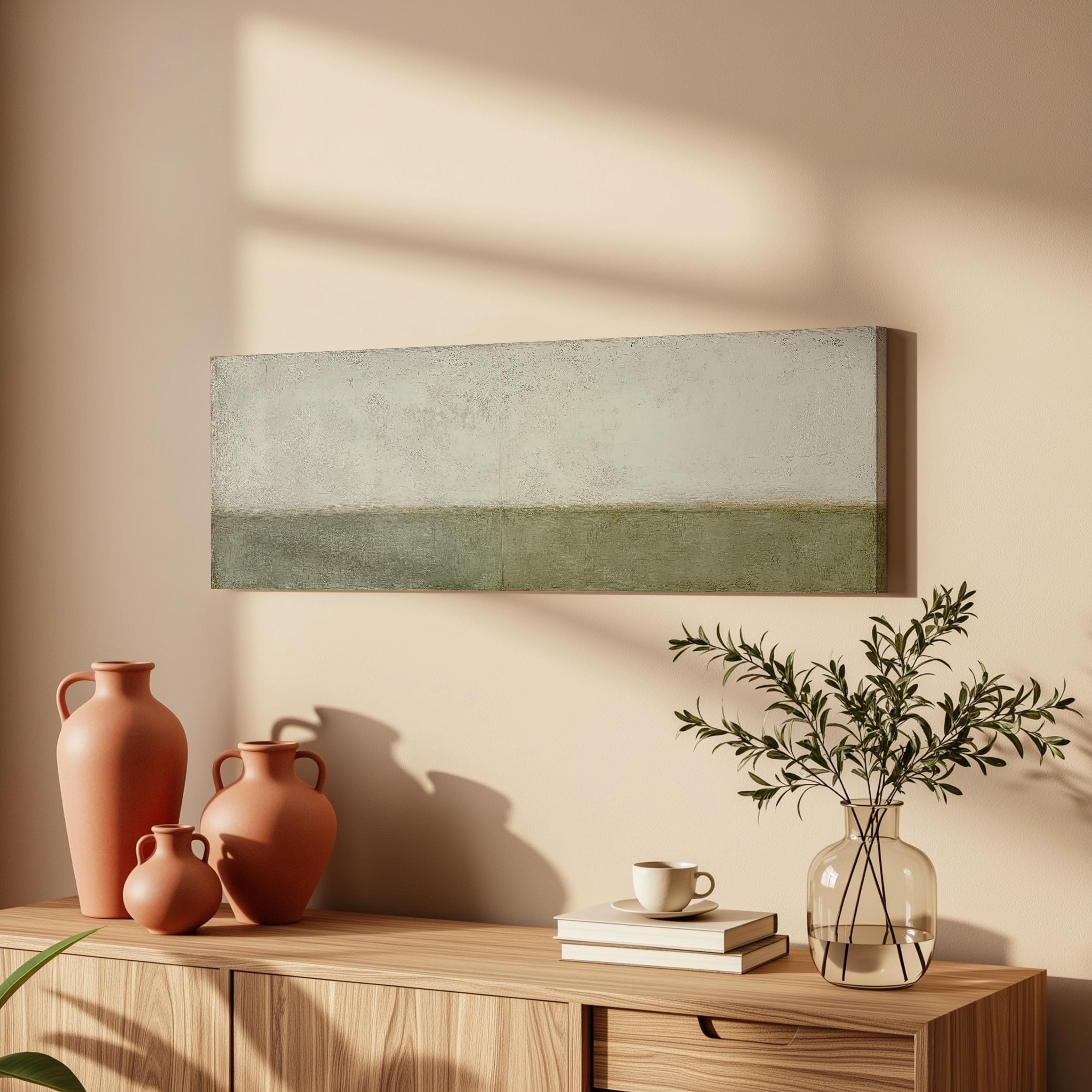 a wooden cabinet with a vase of greenery, a coffee cup, and a stack of books on top. The cabinet is set against a light-colored wall, and a painting is hanging above it.