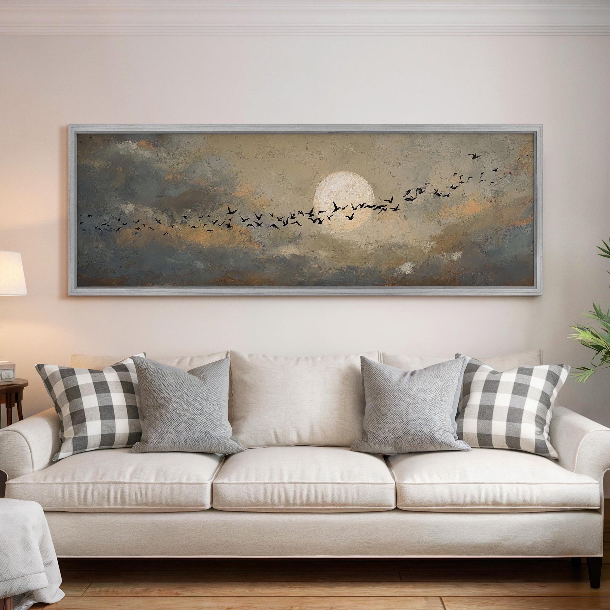 a large painting of a flock of birds flying across a cloudy sky with a full moon in the background, hanging on a wall above a white sofa with patterned throw pillows.