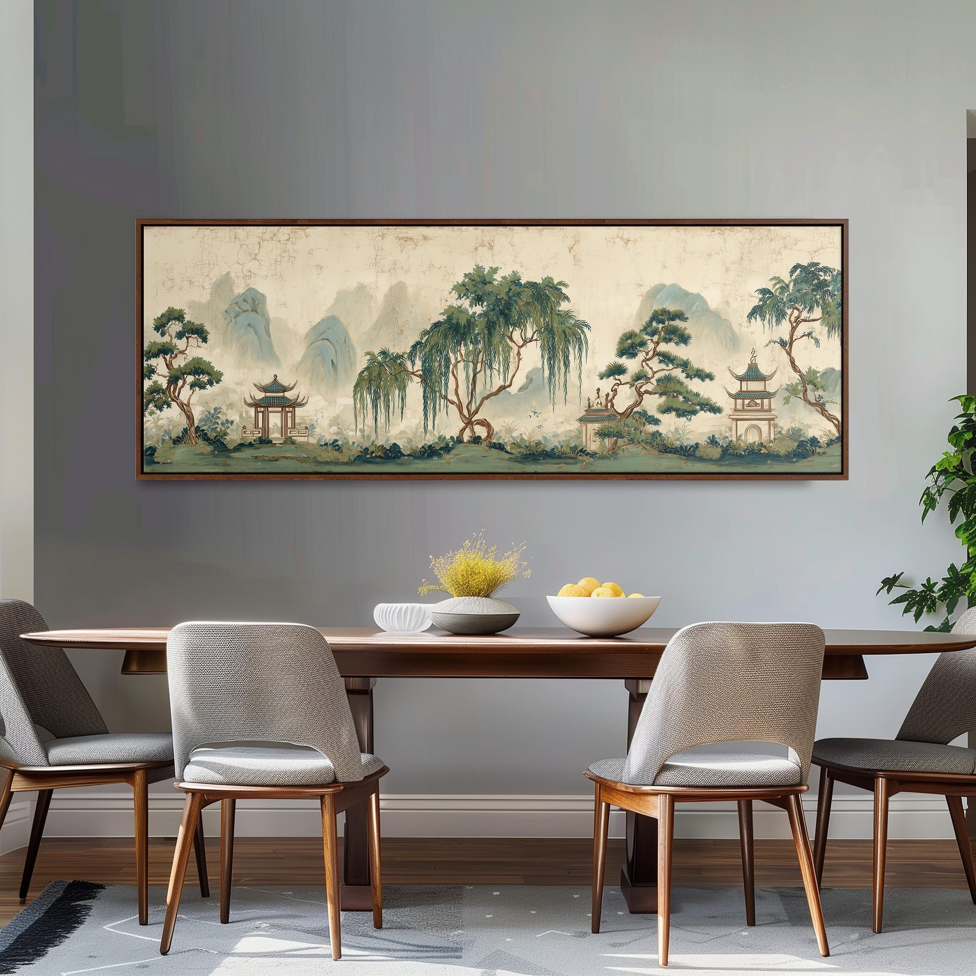 a dining room with a large, framed painting of a serene landscape hanging on the wall above a wooden dining table with four chairs. The painting depicts a tranquil scene with trees, mountains, and pagodas, creating a peaceful and inviting atmosphere.