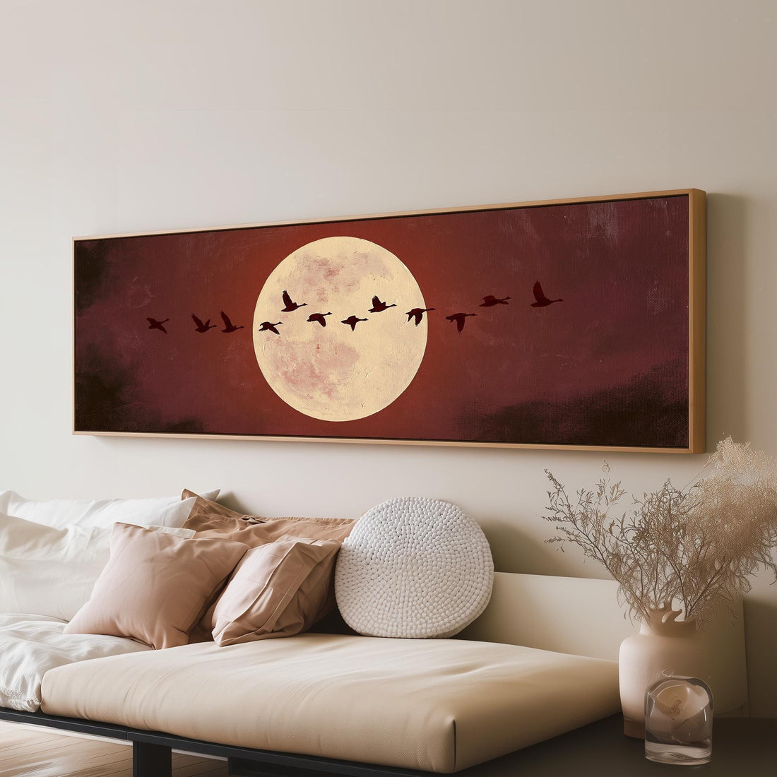 Geese crossing a pale moon on maroon long horizontal canvas print above a sofa in a living room