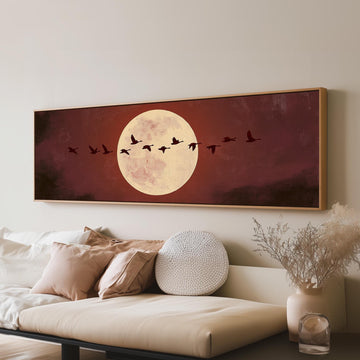 Geese crossing a pale moon on maroon long horizontal canvas print above a sofa in a living room