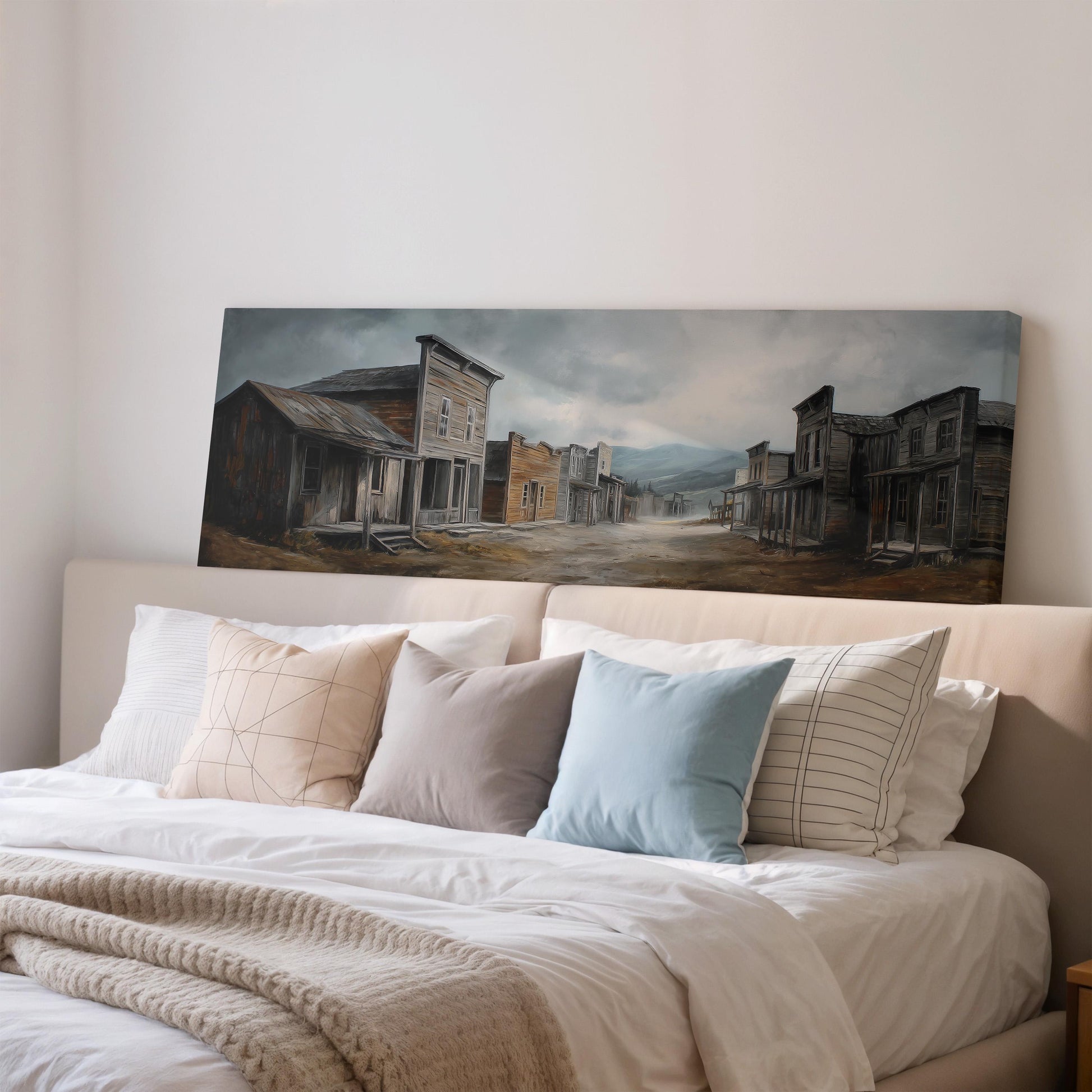 a large painting of a town scene hanging on a wall above a bed with pillows.
