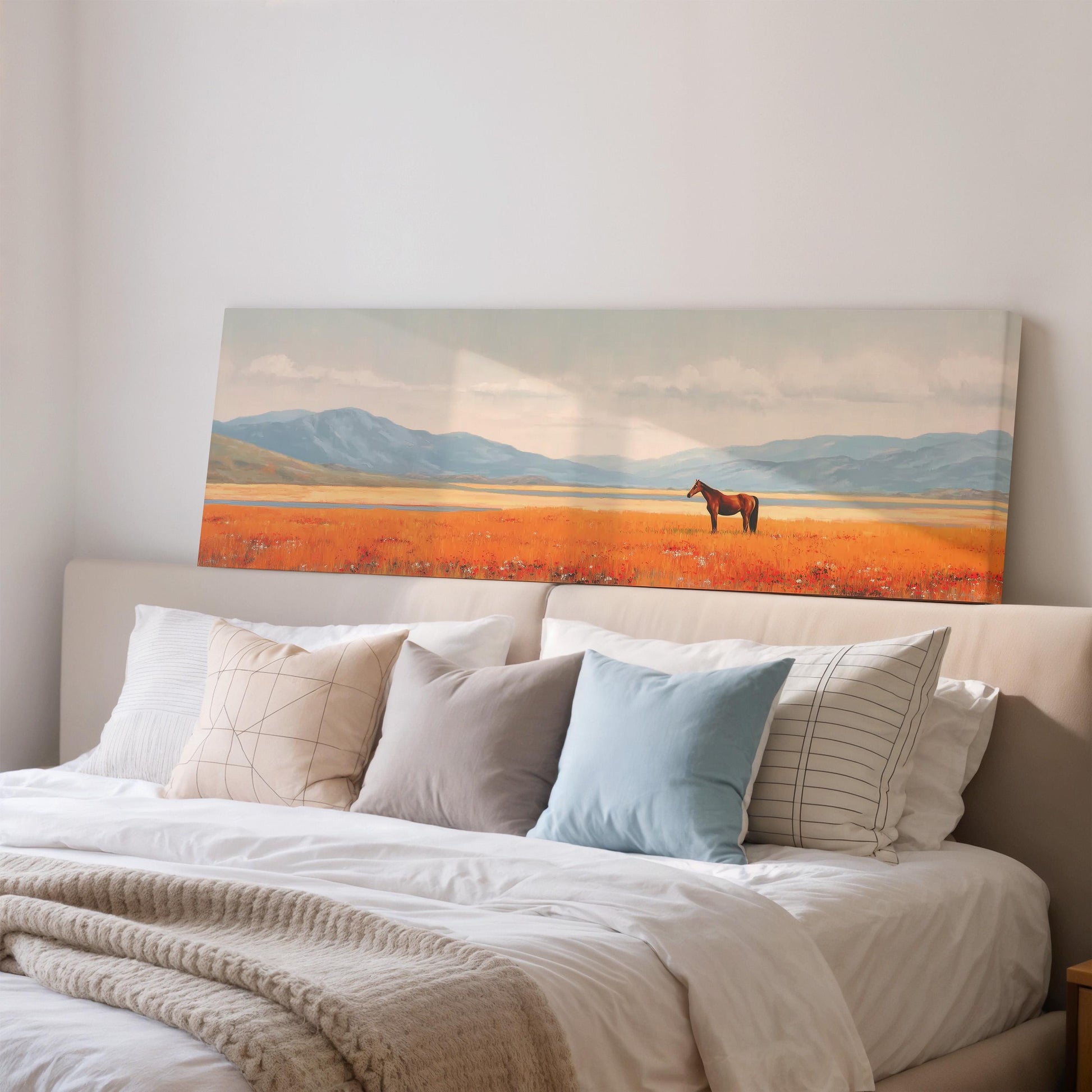 a large painting of a horse in a field, hanging on a wall above a bed with white pillows and a gray blanket.