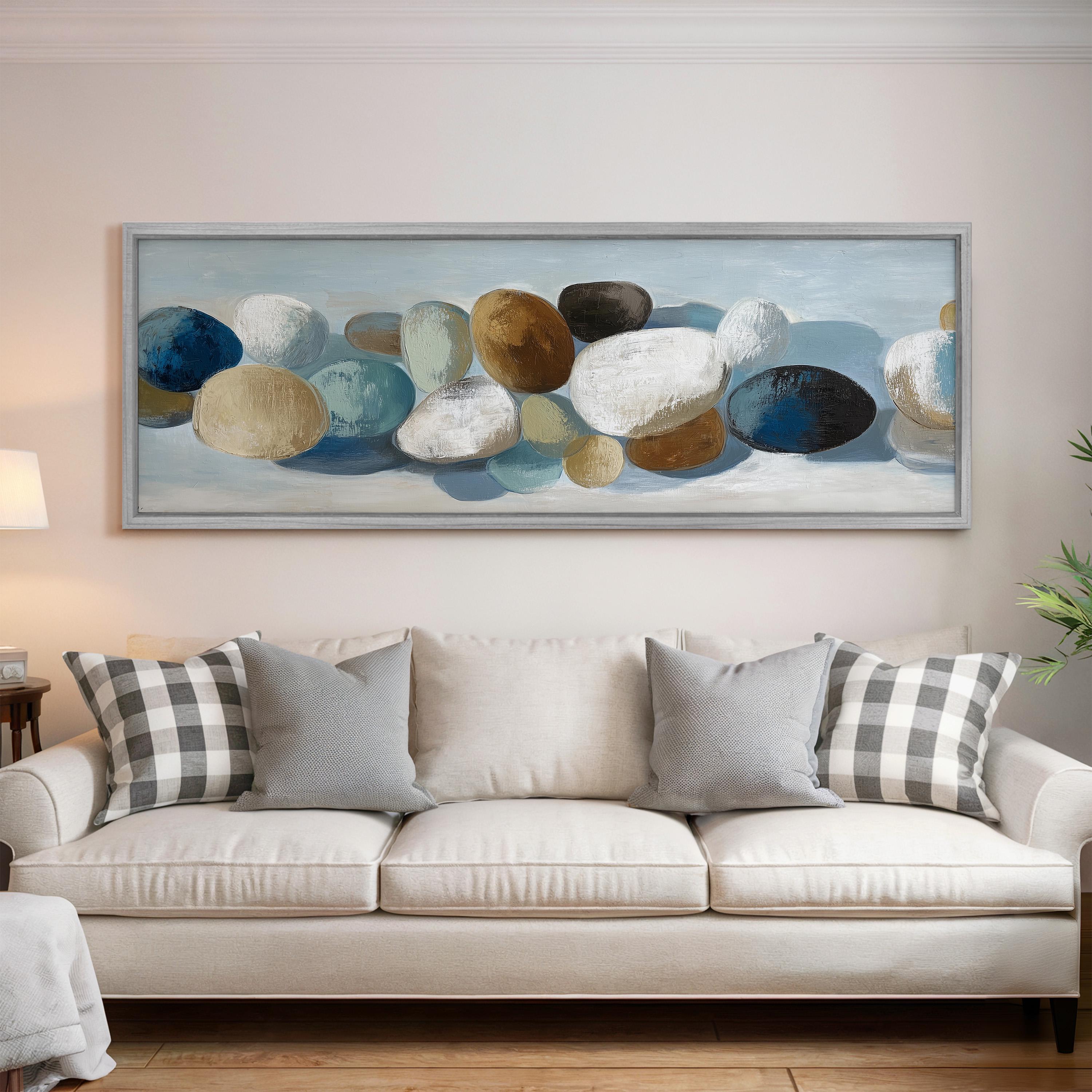 a large painting of rocks hanging on a wall above a white couch with gray and white pillows.