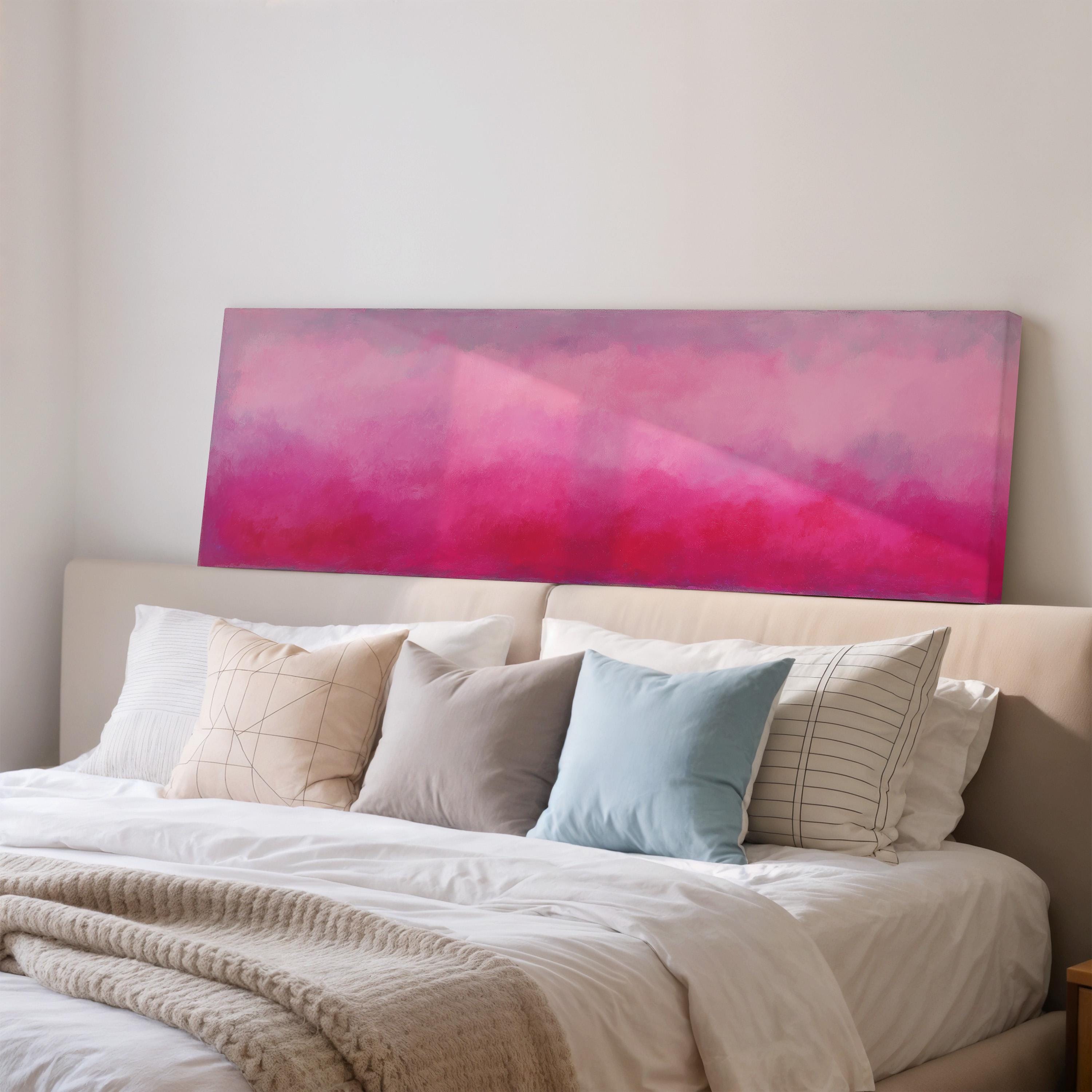 a cozy bedroom with a large bed adorned with white linens and a variety of colorful pillows. Above the bed, there is a large canvas print featuring a vibrant pink and purple gradient background.