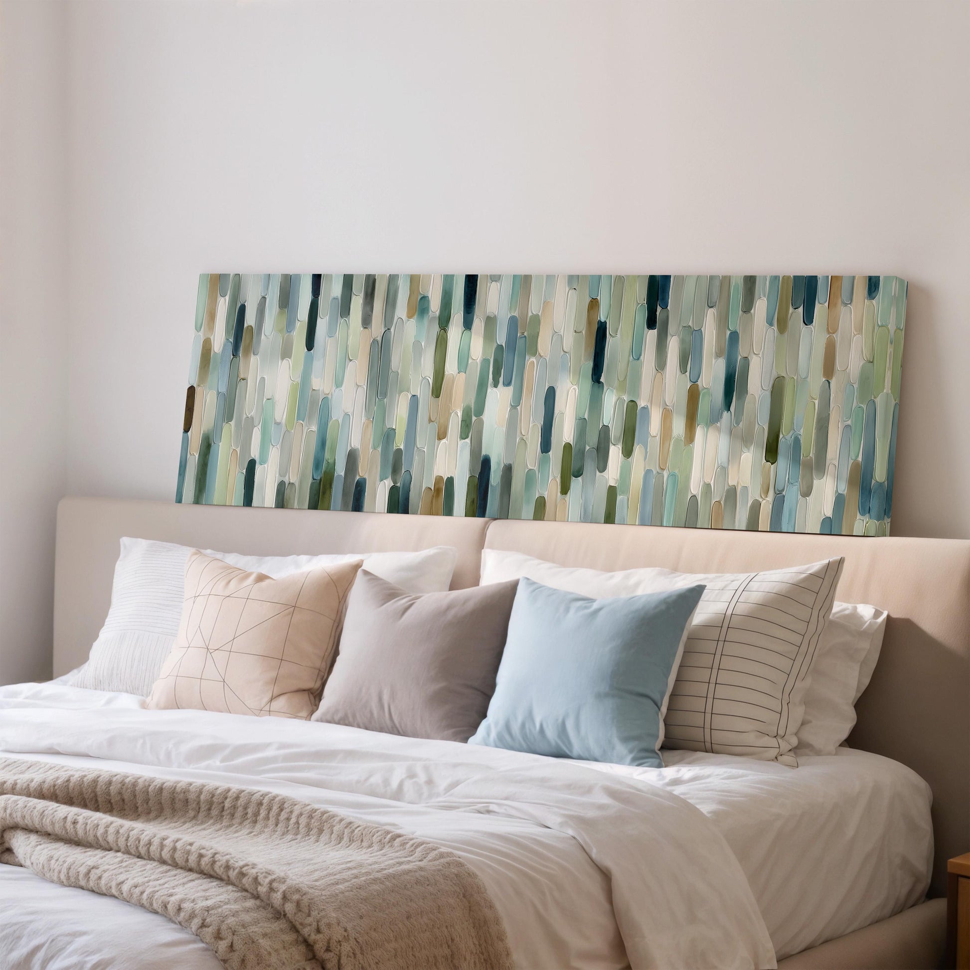 a cozy bedroom with a large bed adorned with white sheets and a variety of colorful throw pillows. Above the bed, there is a large abstract painting with vertical lines in shades of blue, green, and gray.